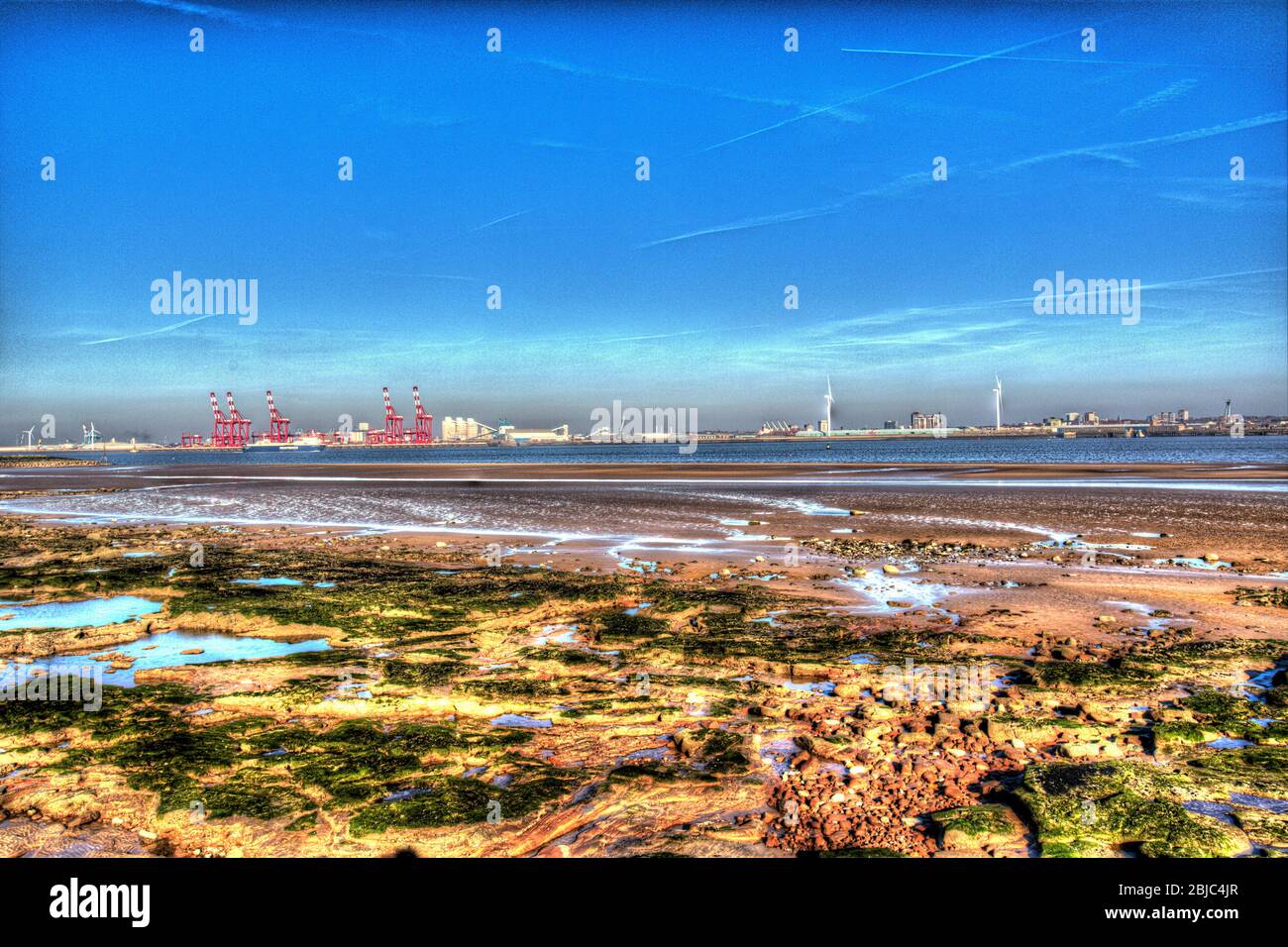 Stadt Wallasey, England. New Brighton Beach mit dem Fluss Mersey und den roten Kränen am Seaforth Container Terminal, im Hintergrund. Stockfoto