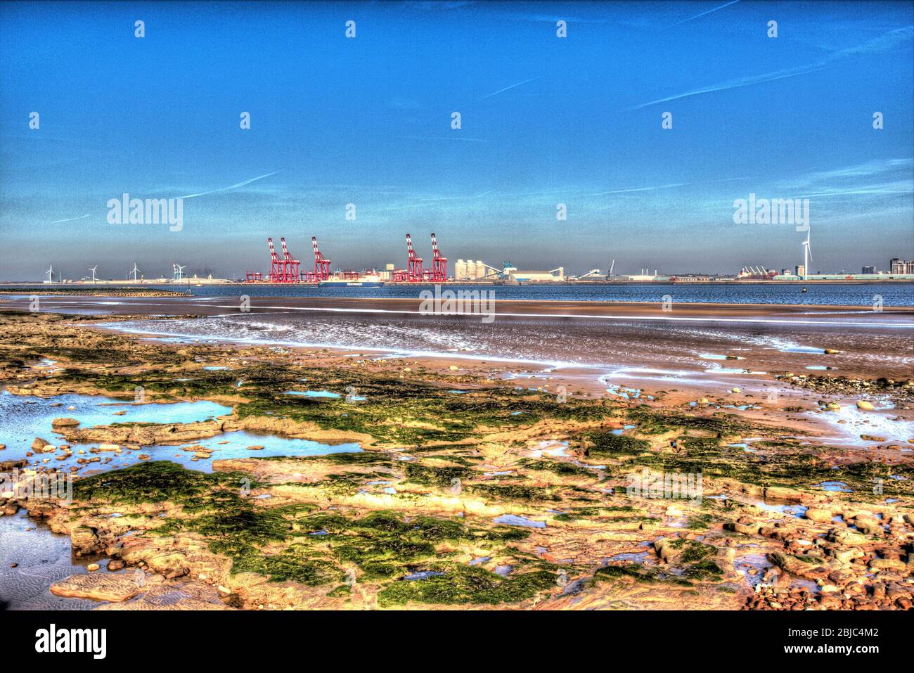 Stadt Wallasey, England. New Brighton Beach mit dem Fluss Mersey und den roten Kränen am Seaforth Container Terminal, im Hintergrund. Stockfoto