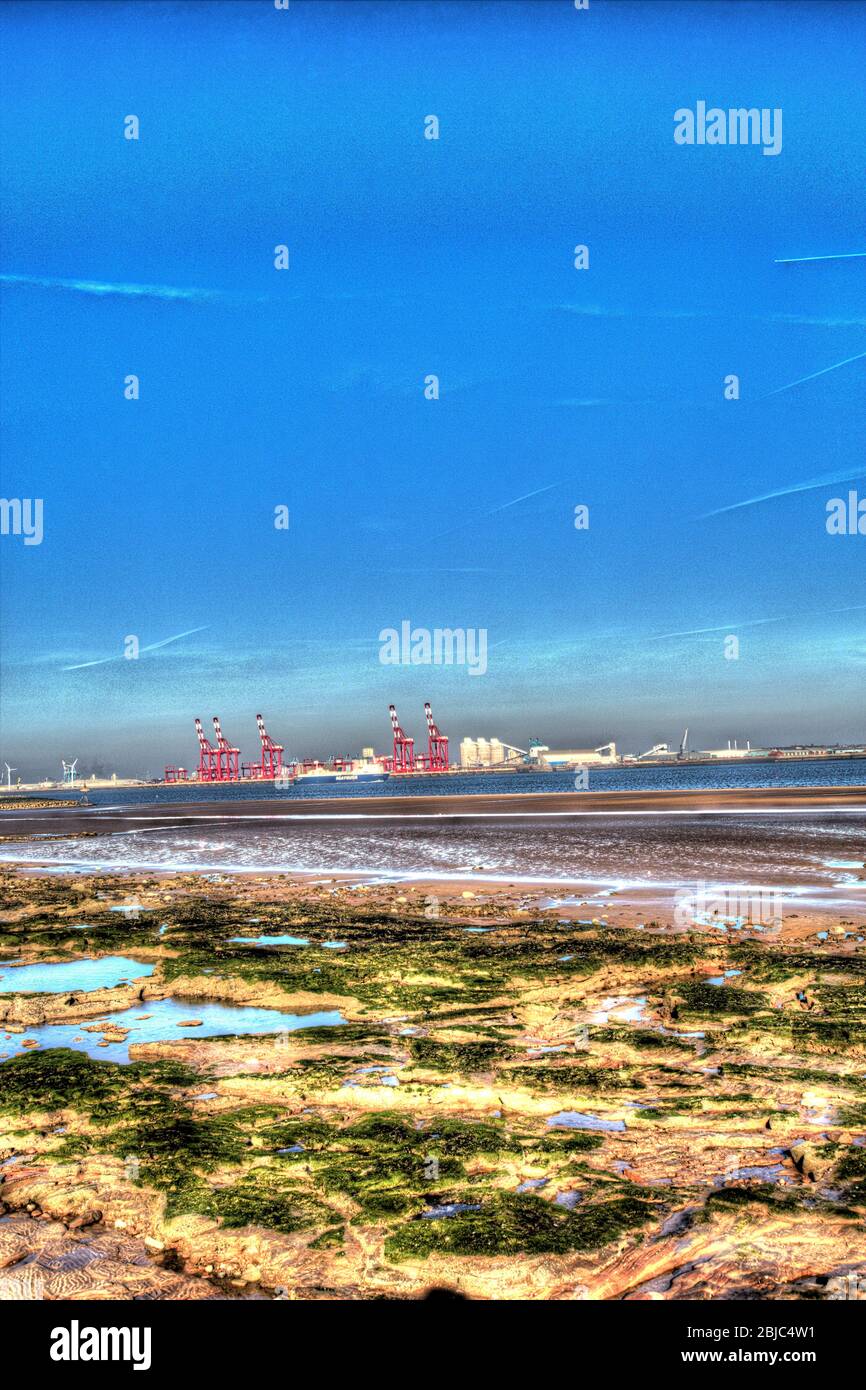 Stadt Wallasey, England. New Brighton Beach mit dem Fluss Mersey und den roten Kränen am Seaforth Container Terminal, im Hintergrund. Stockfoto