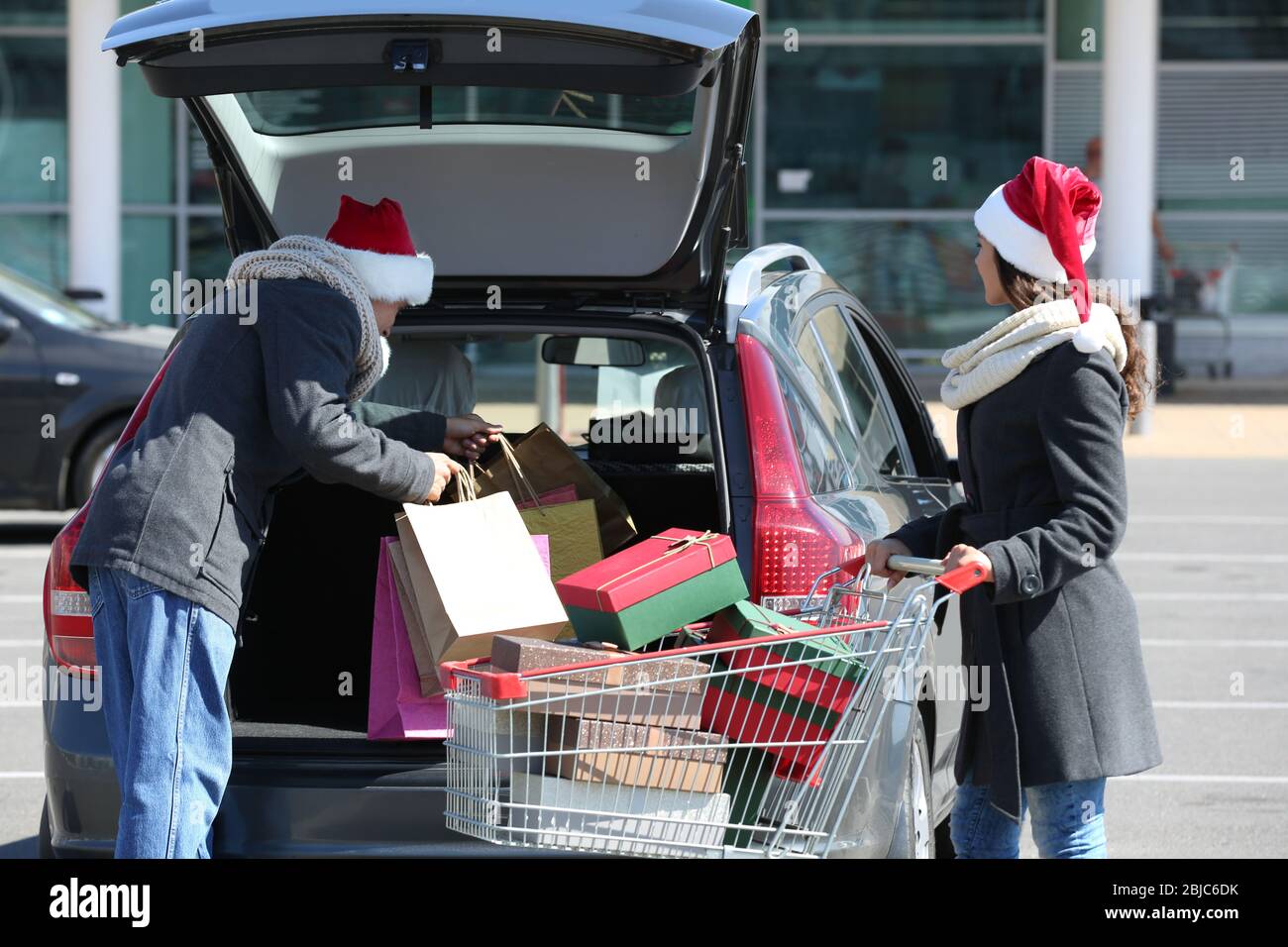 Junges Paar lädt Weihnachtseinkäufe in Autokoffer auf dem Parkplatz des Einkaufszentrums Stockfoto