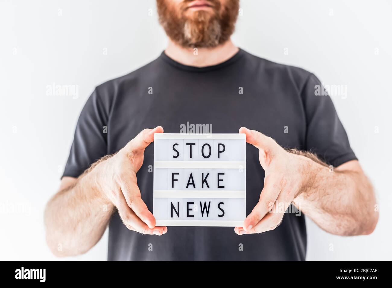 Fake News Infosemics during Covid-19 Pandemie Concept. Mann Hände halten Leuchtkasten mit Text Stoppen Fake News im Vordergrund. Die Leute wollen den Trut kennen Stockfoto