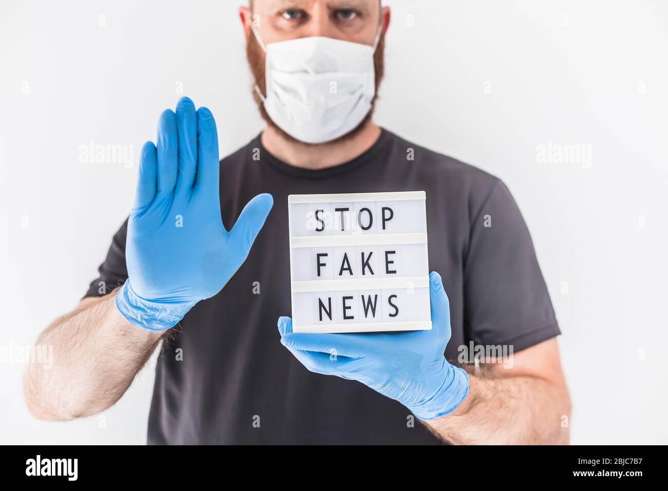 Fake News Infosemics during Covid-19 Pandemie Concept. Mann trägt Schutzmaske und medizinische Handschuhe an den Händen halten Leuchtkasten mit Text Stop Fake ne ne Stockfoto