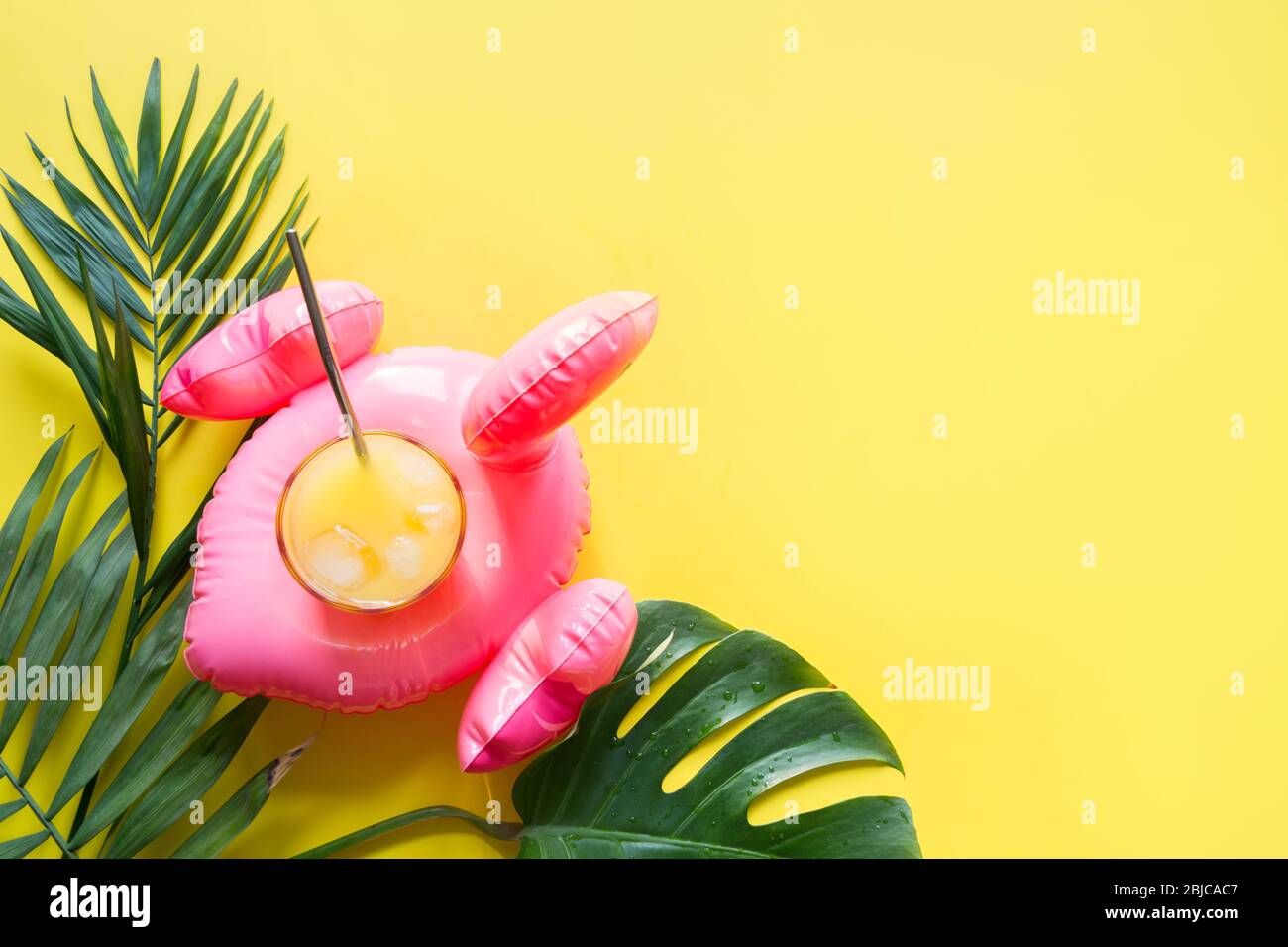 Aufblasbarer rosa Flamingo, Glas Orangensaft, tropische Blätter auf gelbem Hintergrund. Draufsicht. Sommer Strand tropischen Urlaub. Stockfoto
