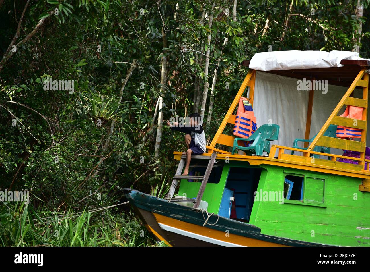 Indonesischer Junge in einem Boot mit einem Schleuder im Dschungel von Kalimantan. Stockfoto