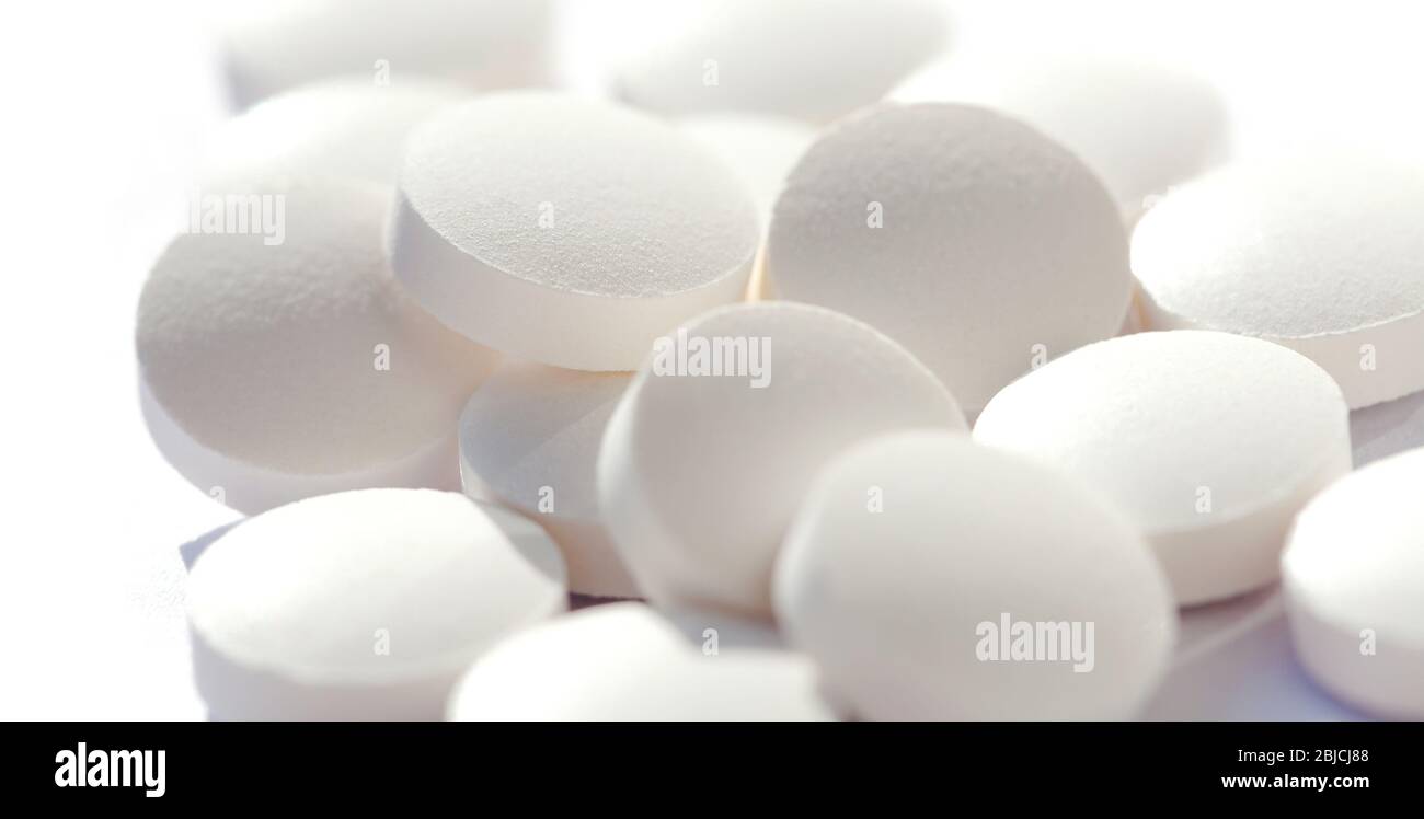 Haufen von einfachen kleinen runden weißen Pillen lose, Gruppe von kleinen Tabletten auf weiß, Makro, Nahaufnahme, konzentrieren sich auf eine Pille. Neue Medikamente, Nahrungsergänzungsmittel und Medikamente Stockfoto
