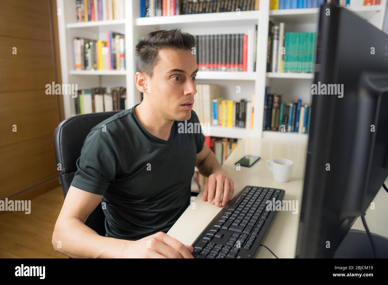 Sitzender Mann in schwarzem Hemd, der auf den Computerbildschirm schaut, sehr überrascht. Mittelaufnahme. Stockfoto
