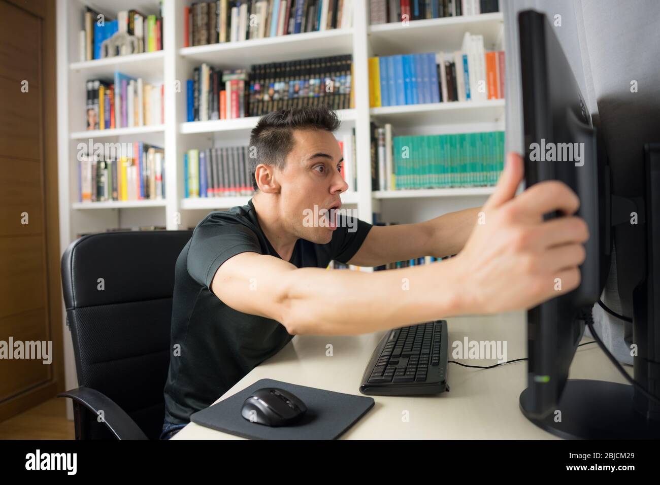 Sitzender Mann in schwarzem Hemd, der auf den Computerbildschirm schaut, sehr überrascht. Mittelaufnahme. Stockfoto