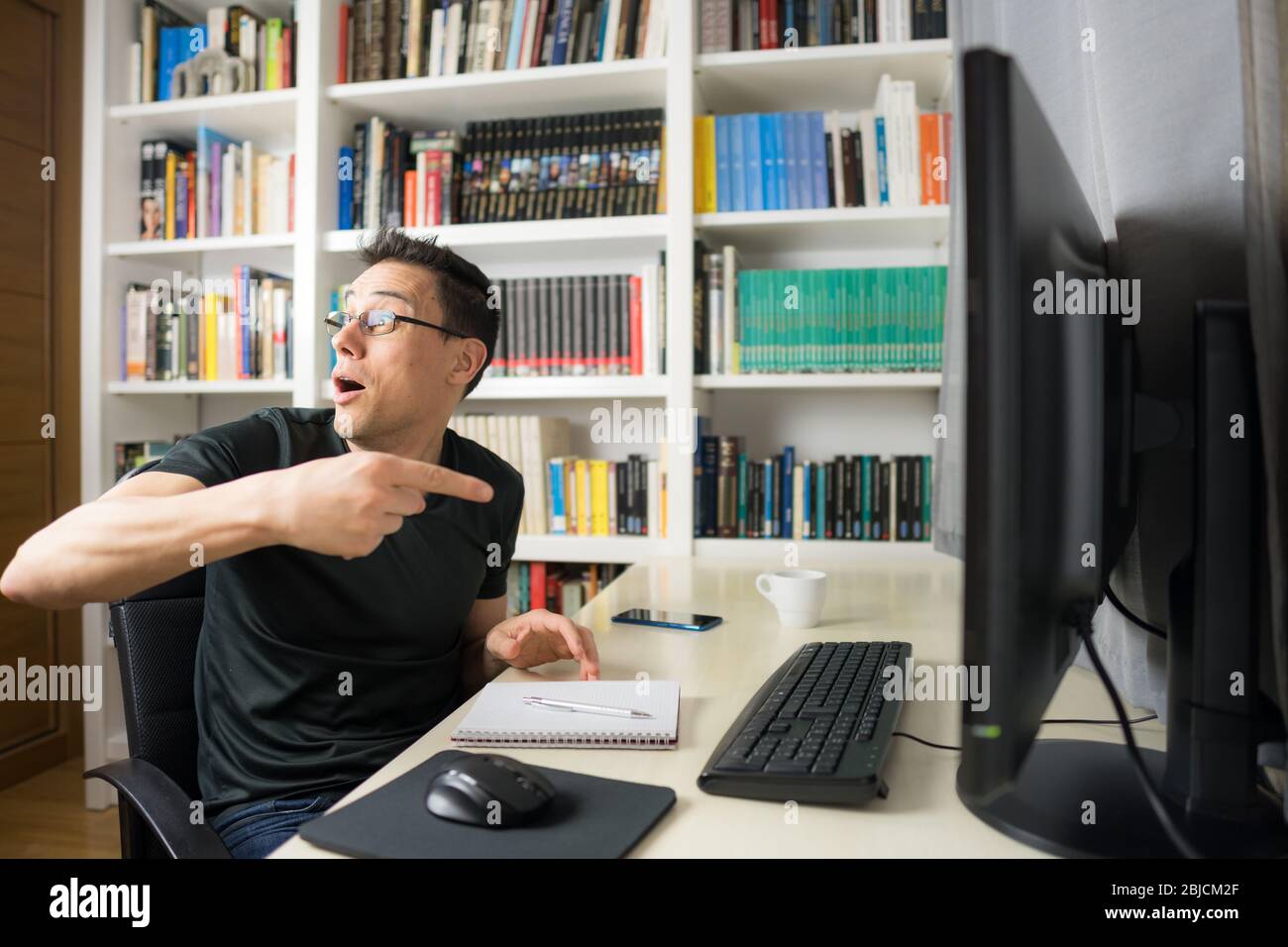 Sitzender Mann in schwarzem Hemd, der auf den Computerbildschirm schaut, sehr überrascht. Mittelaufnahme. Stockfoto
