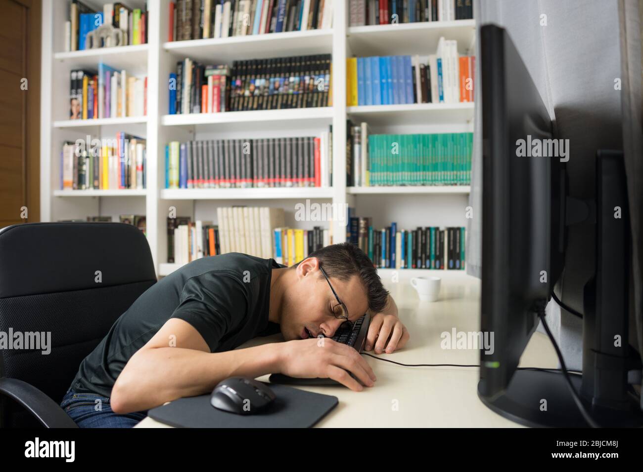 Sitzender Mann in schwarzem Hemd schlafend auf der Computertastatur. Mittelaufnahme. Stockfoto