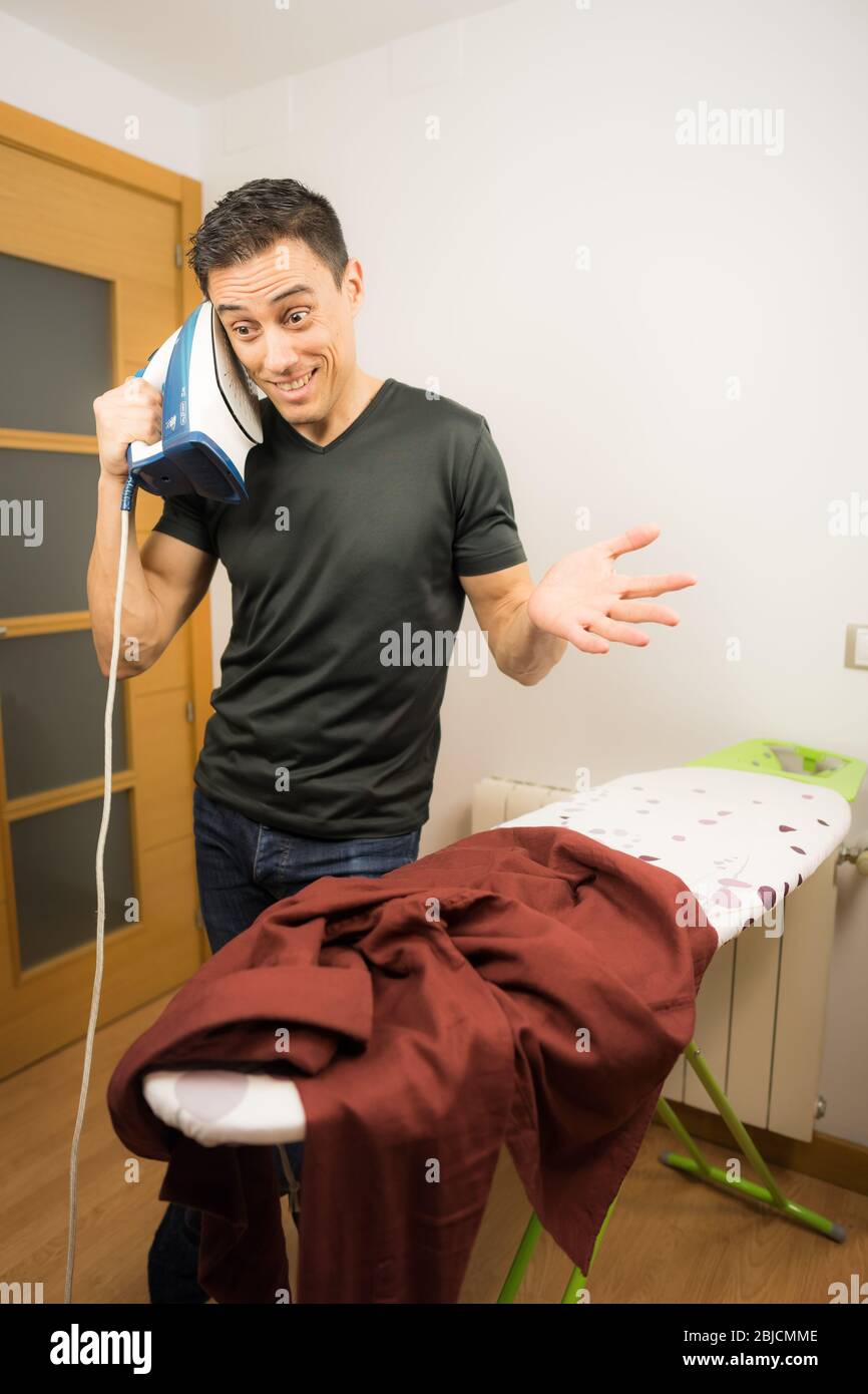 Verrückter Mann, der mit einem Bügeleisen am Telefon telefoniert. Mittelaufnahme. Stockfoto