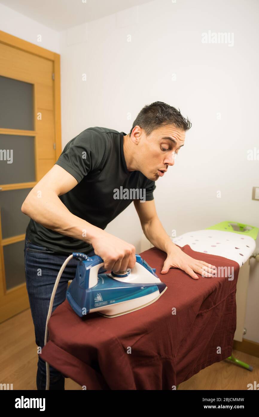 Mann bügelt ein Hemd zu Hause mit äußerster Sorgfalt. Mittelaufnahme. Stockfoto