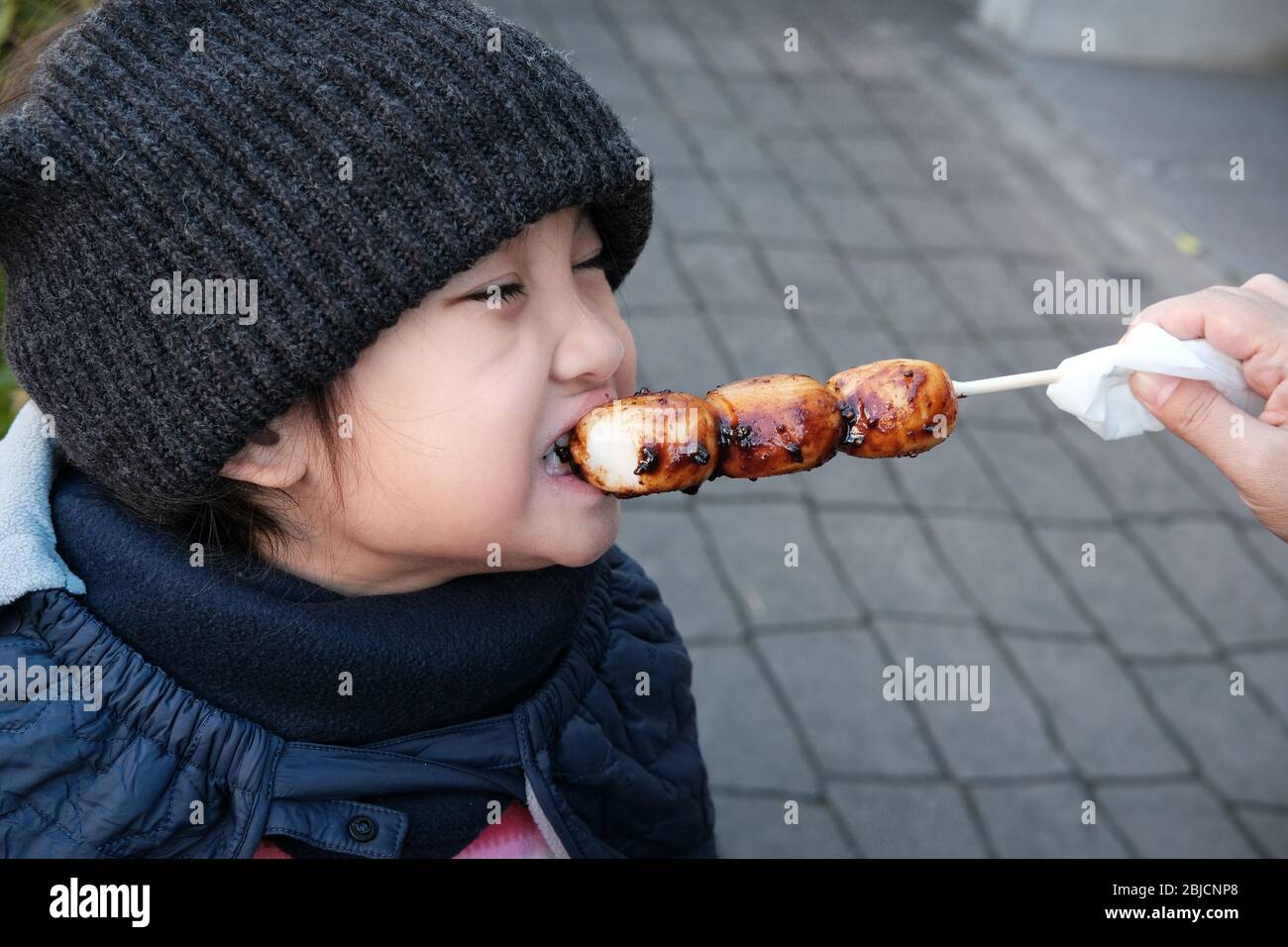Japan, Kid Essen Mitarashi Dango, traditionelle japanische Reis Knödel süße Soja-Glasur. Die Knödel werden auf einem Bambusstock aufgeschwemmt. Traditionelles Japan Stockfoto
