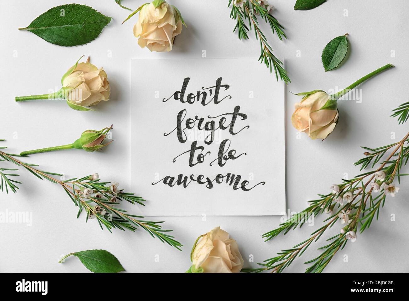 Zitat 'Don't forget to be awesome' auf Papier mit Rosen und Blättern auf weißem Hintergrund geschrieben. Draufsicht Stockfoto