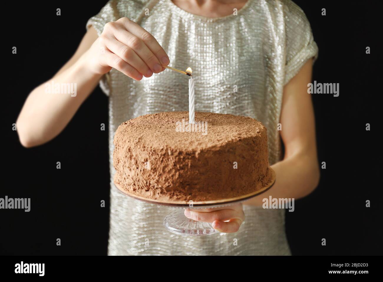 Frau licht Kerze auf Schokolade Kuchen Stockfoto