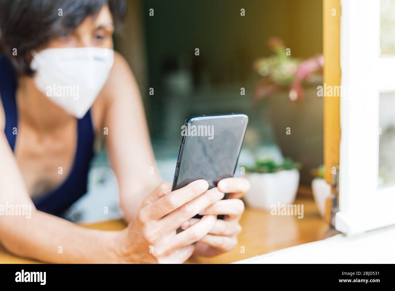 Frau, die aus ihrem Fenster plaudert und während der Quarantäne des Coronavirus eine Maske trägt Stockfoto