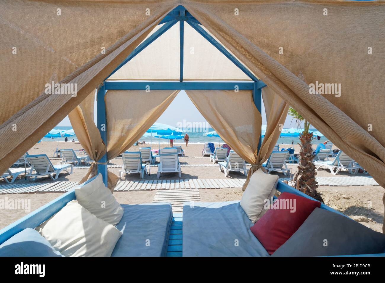 Liegestühle und Urlauber umrahmt von einer Strandhütte. Side Beach, Antalya Türkei Stockfoto