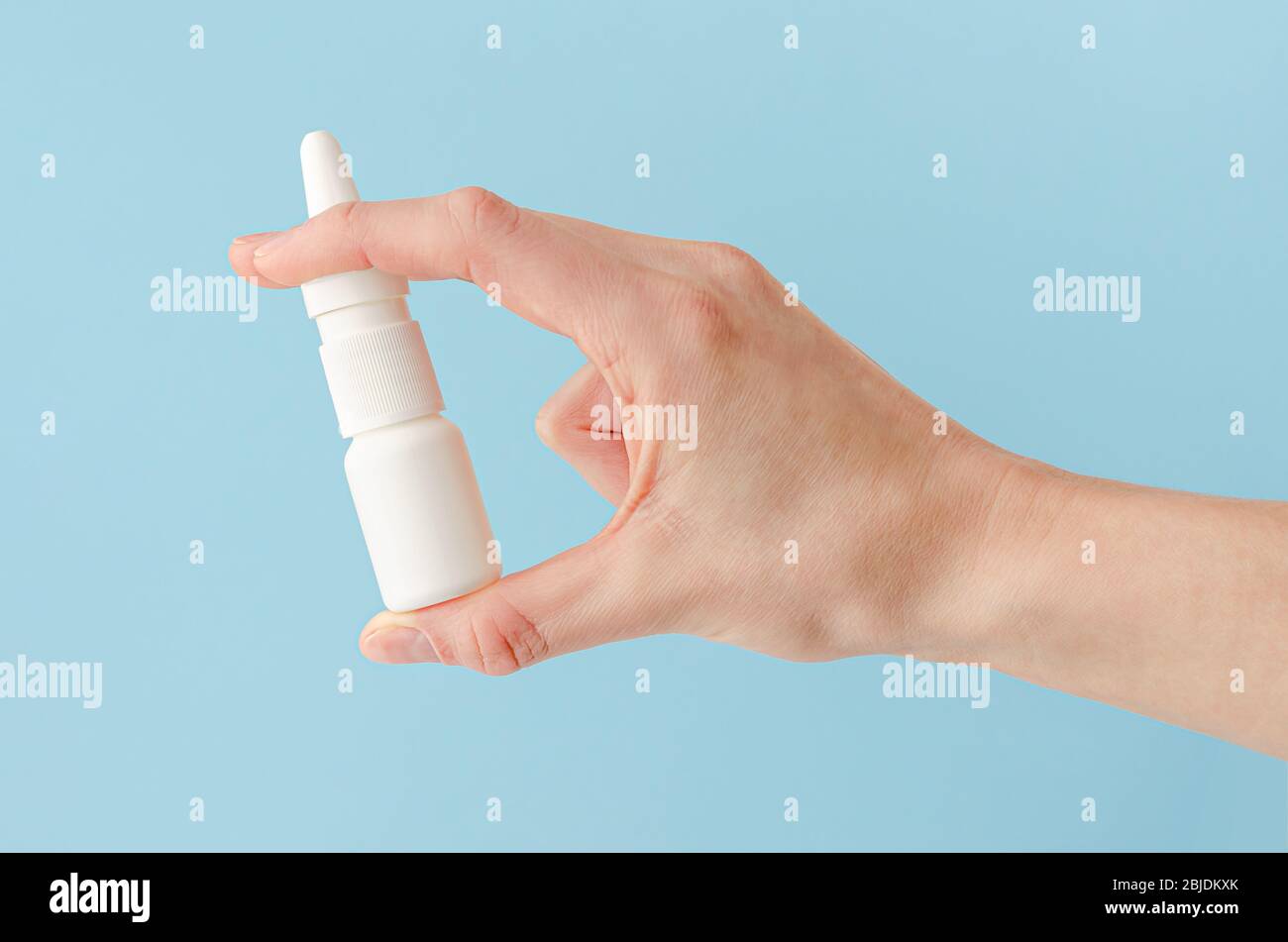 Weibliche Hand hält Nasenspray auf blauem Hintergrund. Saisonale Allergie und allgemeine Kälte Konzept. Stockfoto