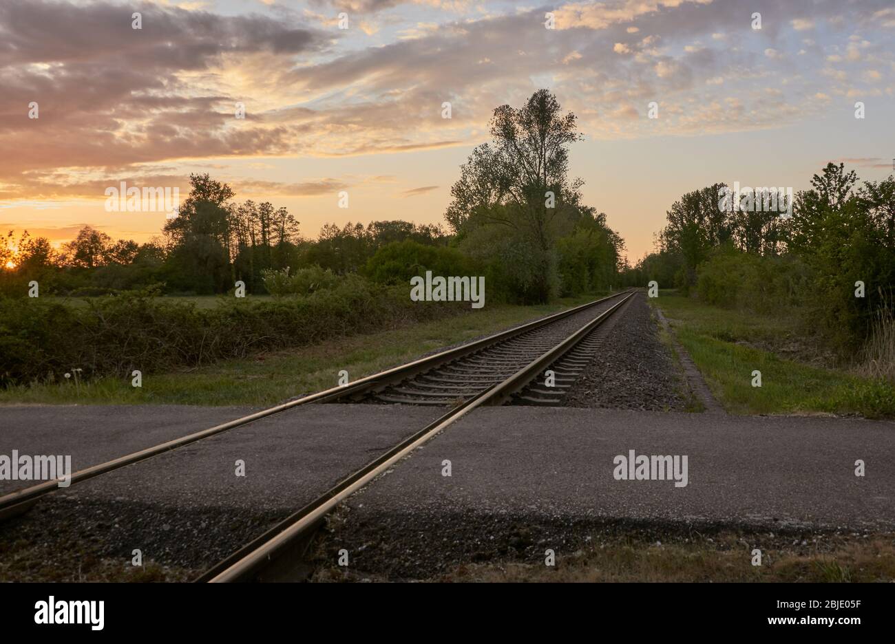 Ungated Eisenbahnübergang und eine ländliche Landschaft gegen den Sonnenuntergang Himmel. Hintergrund für Schienenverkehr und Infrastruktur Stockfoto