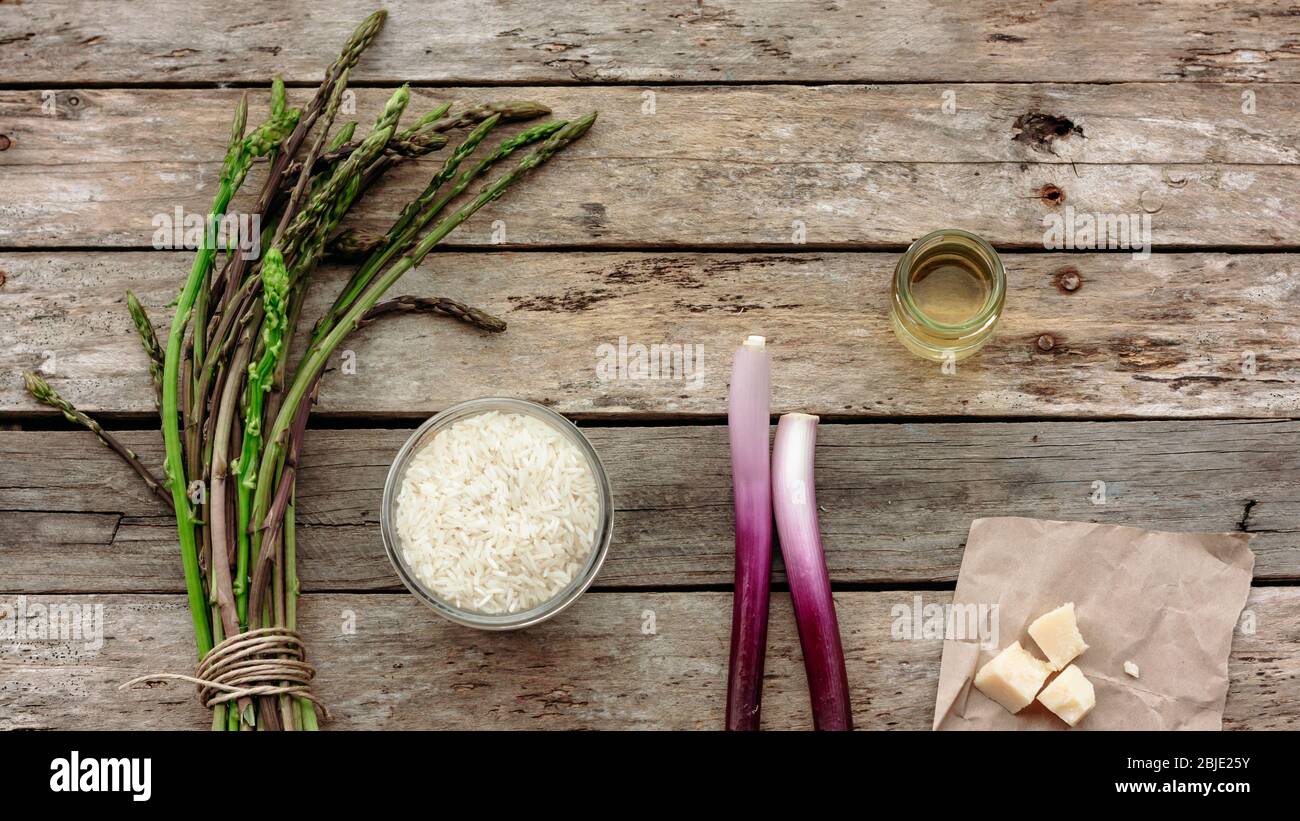 Zutaten für italienisches Risotto auf Holztisch: Reis, Wildspargel, Parmesan, grüne Zwiebeln, Schalotten oder Schalotten. Draufsicht, Platz für Text Stockfoto