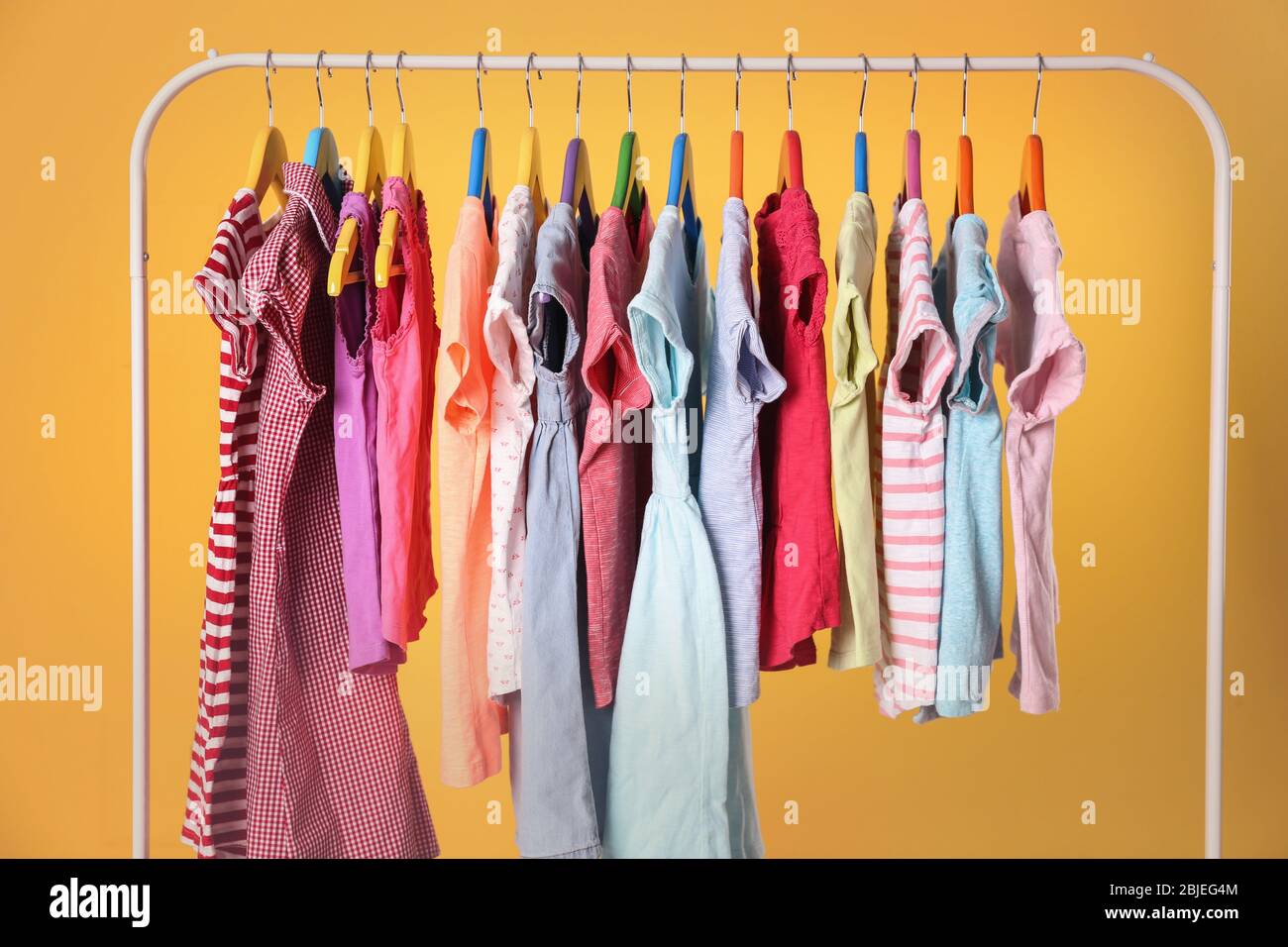 Kleiderbügel mit bunten Kleidern auf gelbem Hintergrund Stockfoto