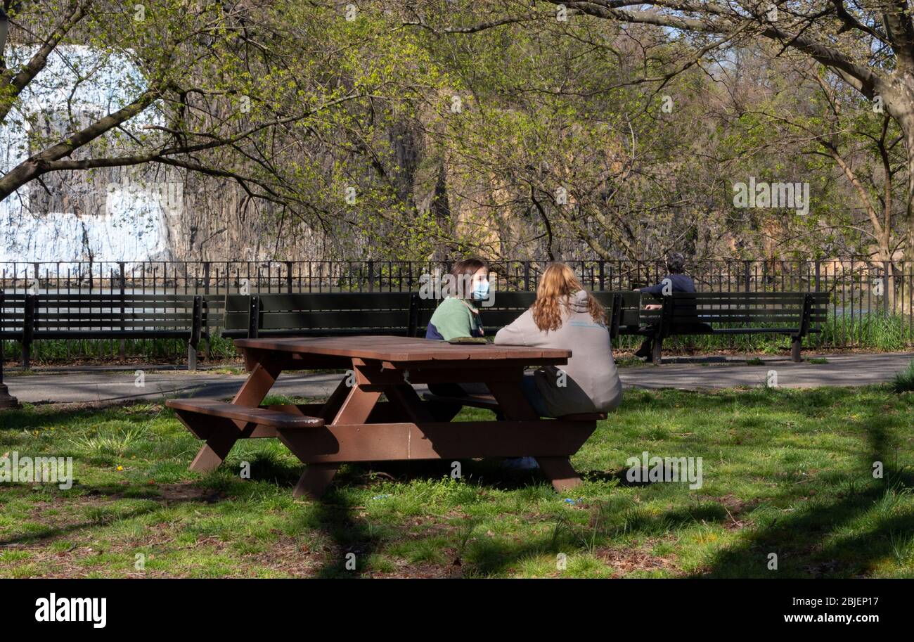 Eine Frau, die mit einem Freund auf einem Picknicktisch im Inwood Hill Park spricht, während sie eine Gesichtsmaske trägt, ein Symbol des Lebens im Coronavirus oder der Covid-19-Pandemie Stockfoto