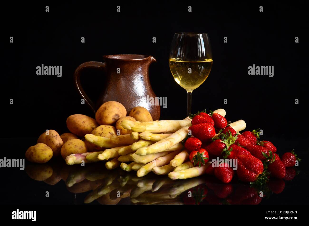 Spargel, Kartoffeln und Erdbeeren vor schwarzem Hintergrund, mit einem Glas Wein, einem Glas und einer Kerze, wie ein Stillleben, wie eine Farbe Stockfoto
