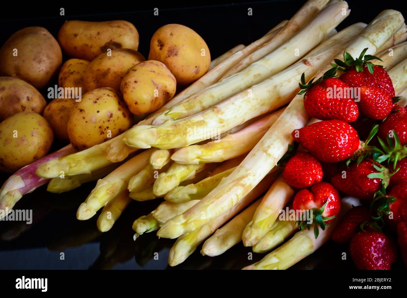 Spargel, Kartoffeln und Erdbeeren vor schwarzem Hintergrund wie ein Stillleben, wie ein Gemälde eines alten Künstlers Stockfoto