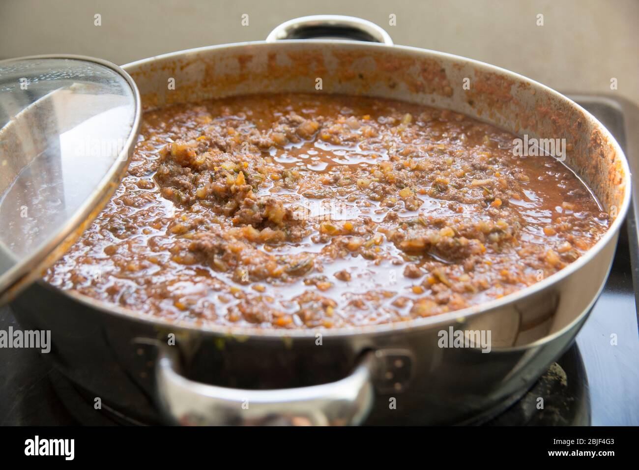 Draufsicht auf eine hausgemachte Bolognese-Sauce (ragù alla Bolognese) mit frischem Basilikum (Ocimum Basilicum) in einem Topf. Stockfoto