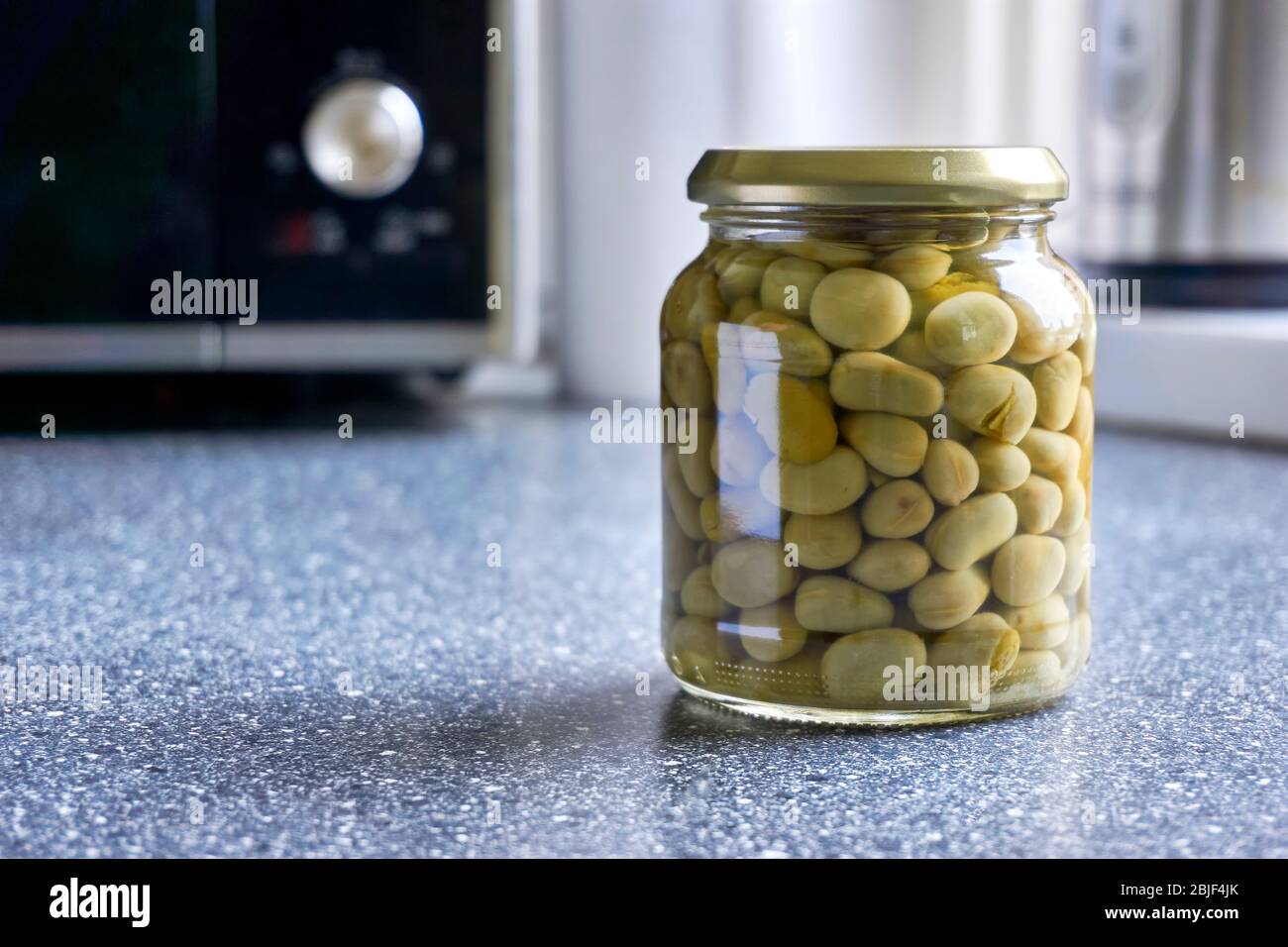 Ein Glas mit Dosenbohnen auf der Küchenplatte mit Mikrowelle. Bild mit Kopierbereich und selektivem Fokus. Stockfoto