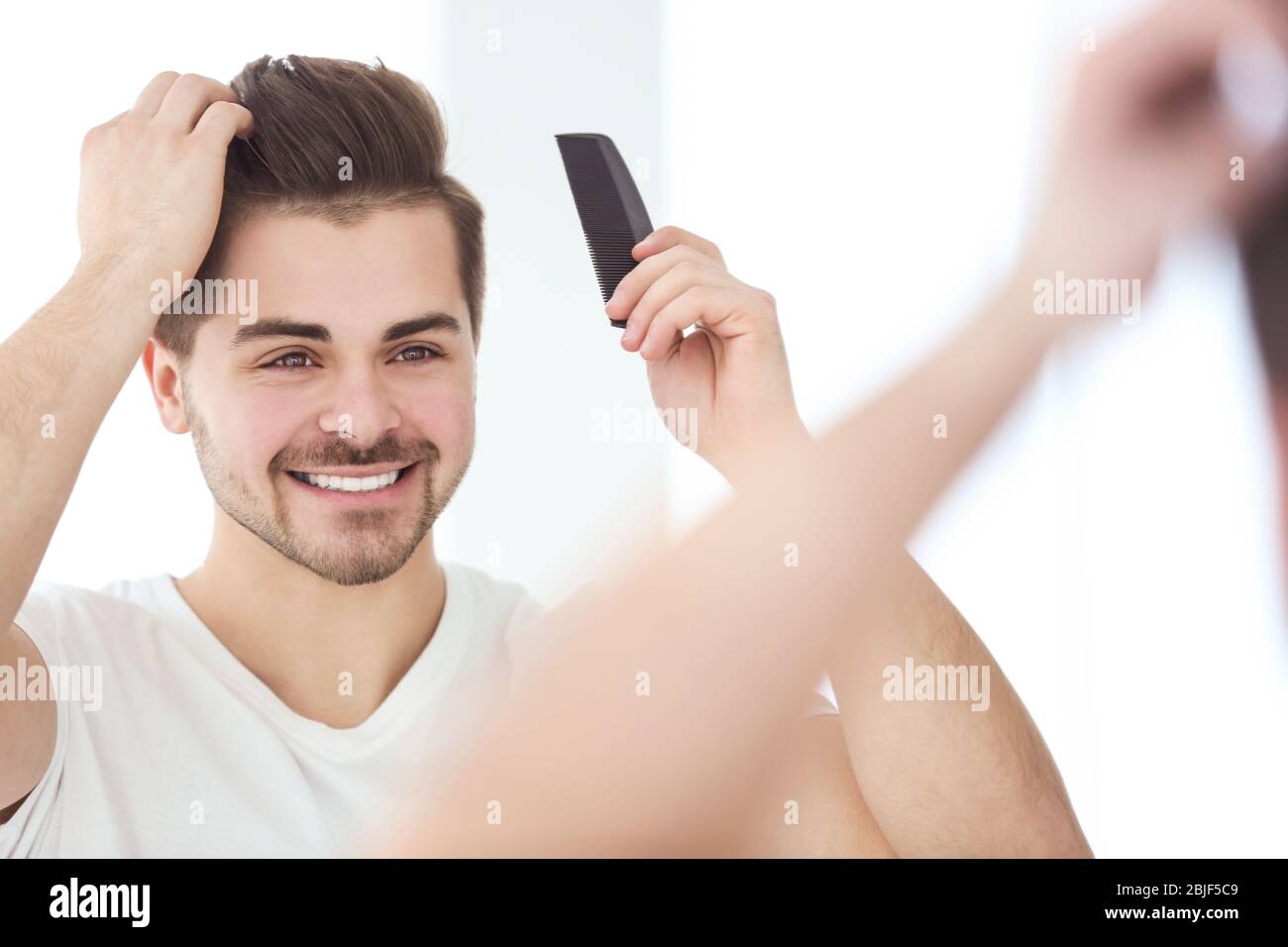 Ein hübscher junger Mann, der vor dem Spiegel die Haare kämmt Stockfoto