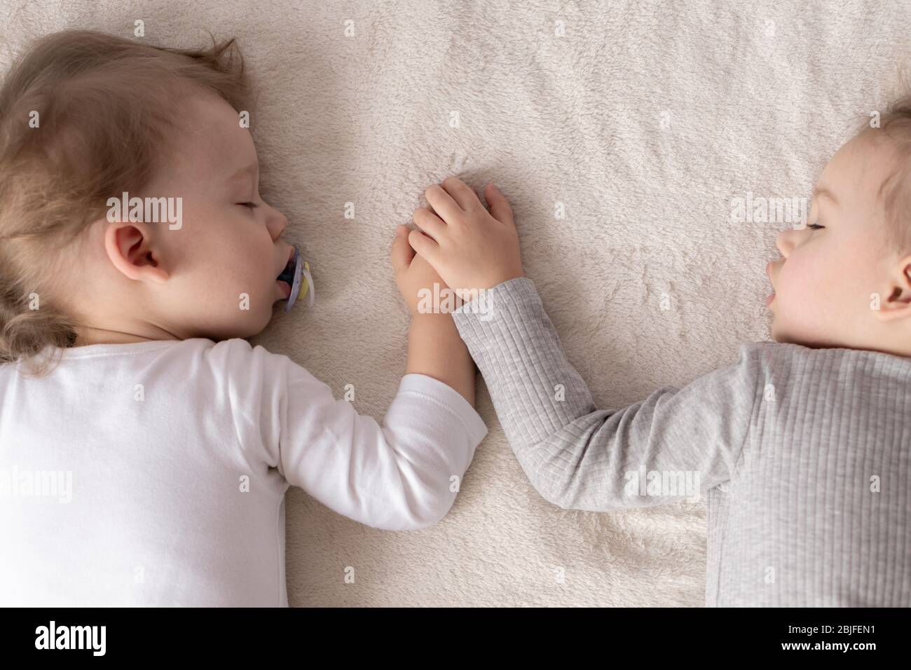 Kindheit, Schlaf, Entspannung, Familie, Lifestyle-Konzept - zwei kleine Kinder im Alter von 2 und 3 Jahren in weiß-beigem Body schlafen auf einem beige Stockfoto