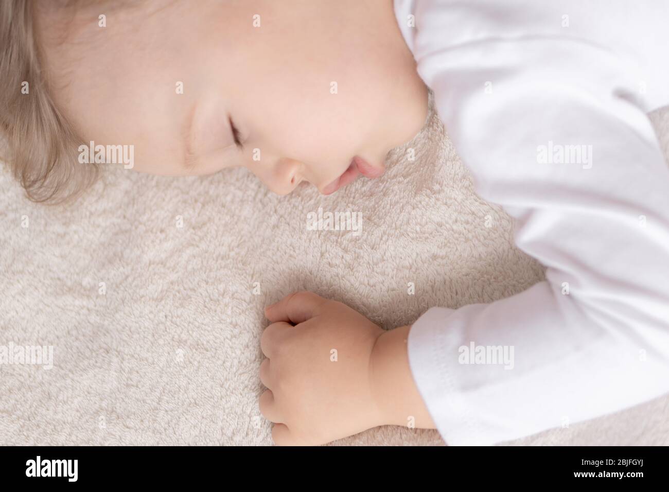Kindheit, Schlaf, Ruhe, Familie, Lifestyle-Konzept - Nahaufnahme Porträt eines süßen kleinen Jungen von 2 Jahren in einem weißen Körper schläft auf einem beigen Bett bei Stockfoto