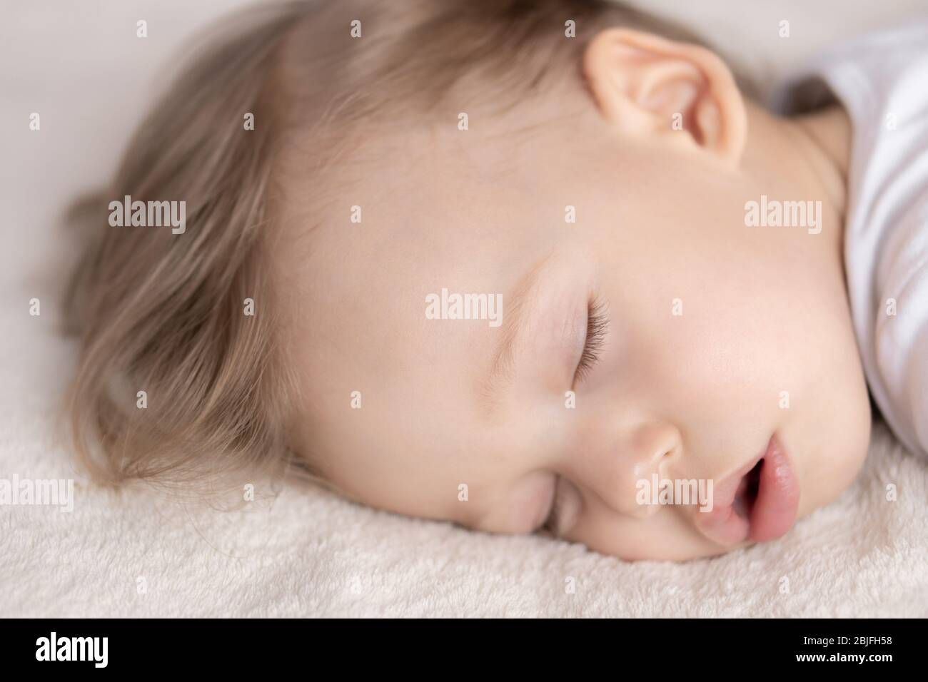 Kindheit, Schlaf, Ruhe, Familie, Lifestyle-Konzept - Nahaufnahme Porträt eines süßen kleinen Jungen von 2 Jahren in einem weißen Körper schläft auf einem beigen Bett bei Stockfoto