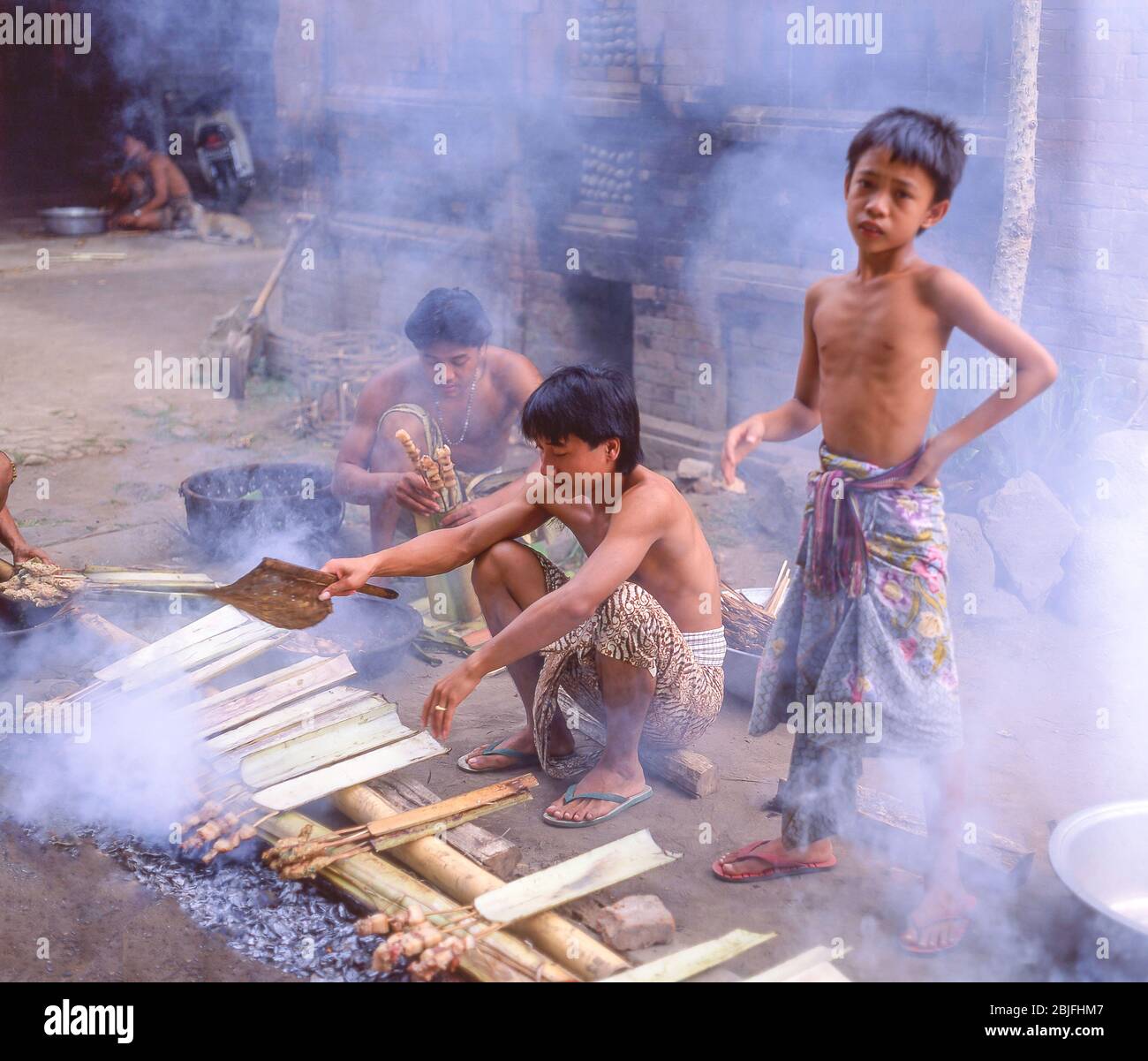 Junge Dorfjungen kochen am offenen Feuer, Tenganan Ancient Village, Tenganan, Bali, Republik Indonesien Stockfoto