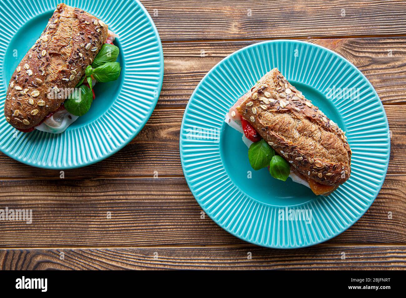 Sandwiches mit italienischem Prosciutto und Basilikumblättern auf rustikalem Holzhintergrund, türkisfarbene Teller, Draufsicht. Stockfoto