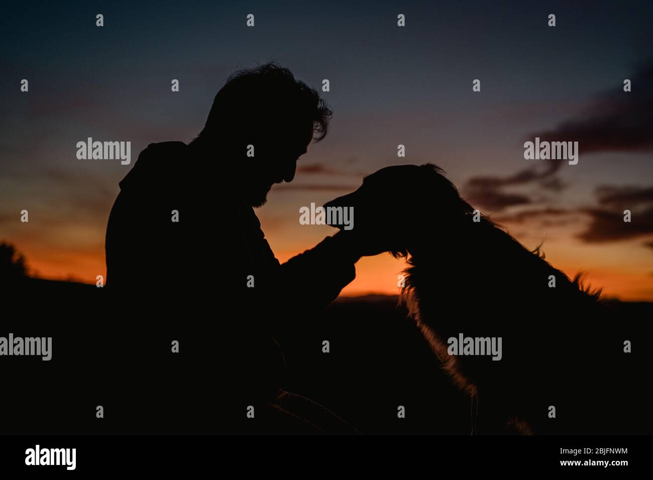 Mann, der Hund bei Sonnenuntergang ansieht Stockfoto