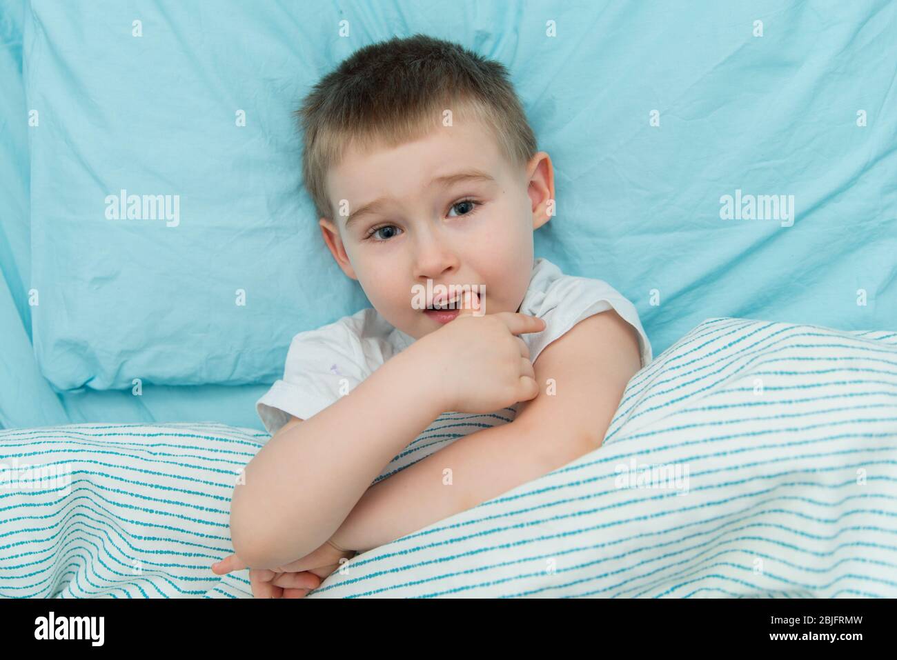 Nachdenklich liebenswert junge in weißem Hemd legt sich im Bett unter der Decke Stockfoto