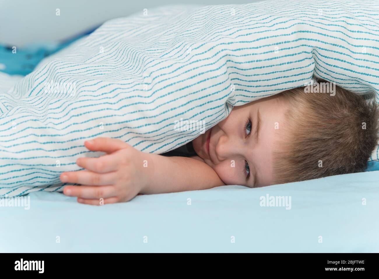 Der kleine Junge liegt unter der Decke und lächelt. Nahaufnahme niedlichen Kleinkind Porträt Stockfoto