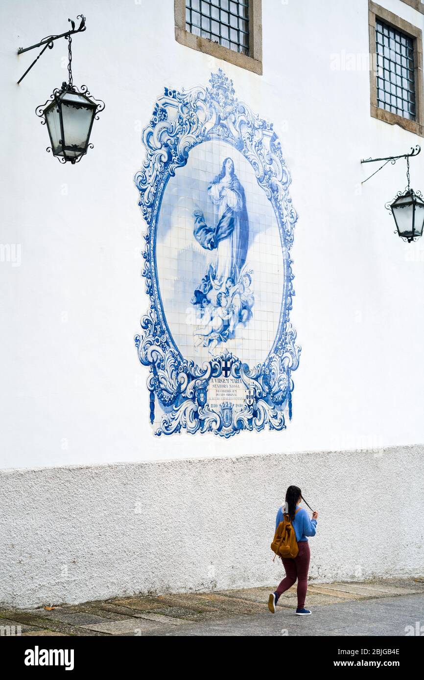 Junge Frau, die blaue und weiße Azulejos Keramikfliesen der Kirche von Carmo in Guimares im Norden Portugals passiert Stockfoto