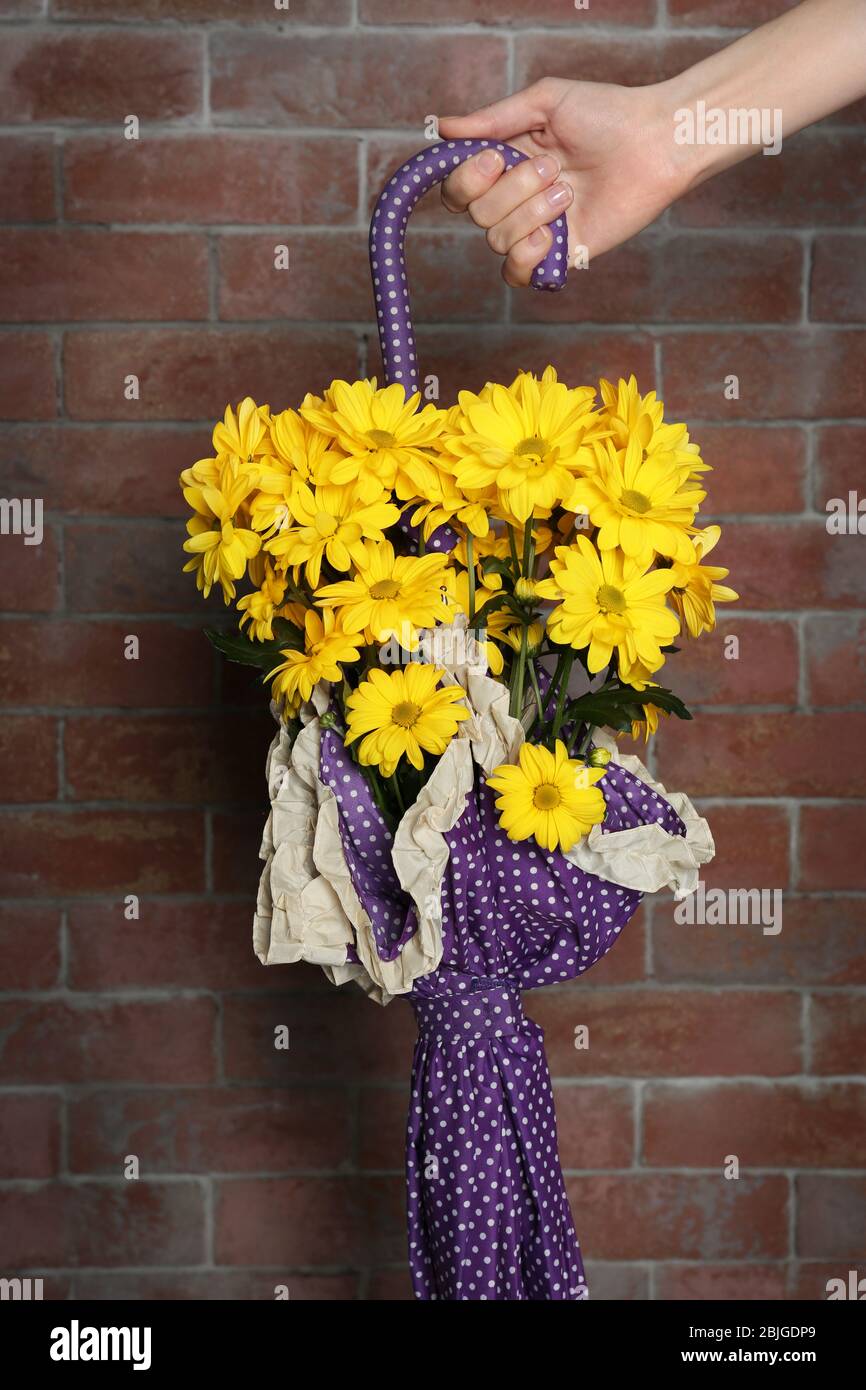 Frau mit lila Farbe Regenschirm mit schönen Blumen auf Backstein Wand Hintergrund Stockfoto