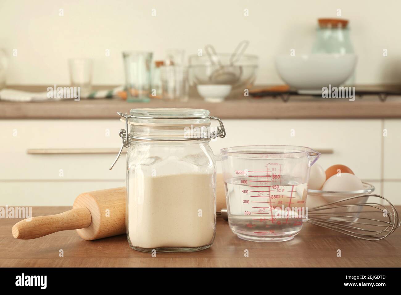 Mehl im Glas und Zutaten für Teig auf dem Tisch Stockfoto