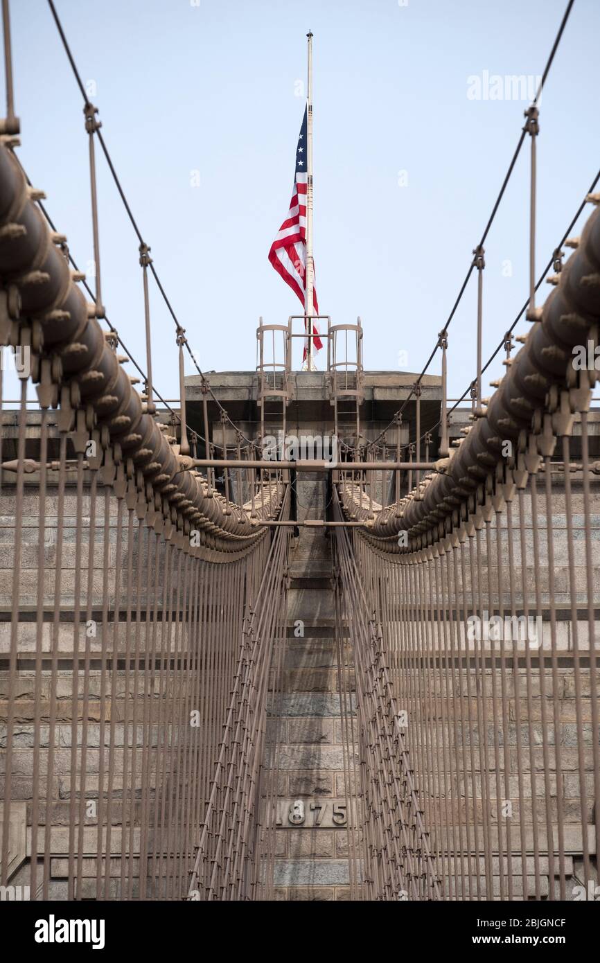 Detail von Drähten und Turm mit amerikanischer Flagge auf der historischen Brooklyn Bridge Stockfoto