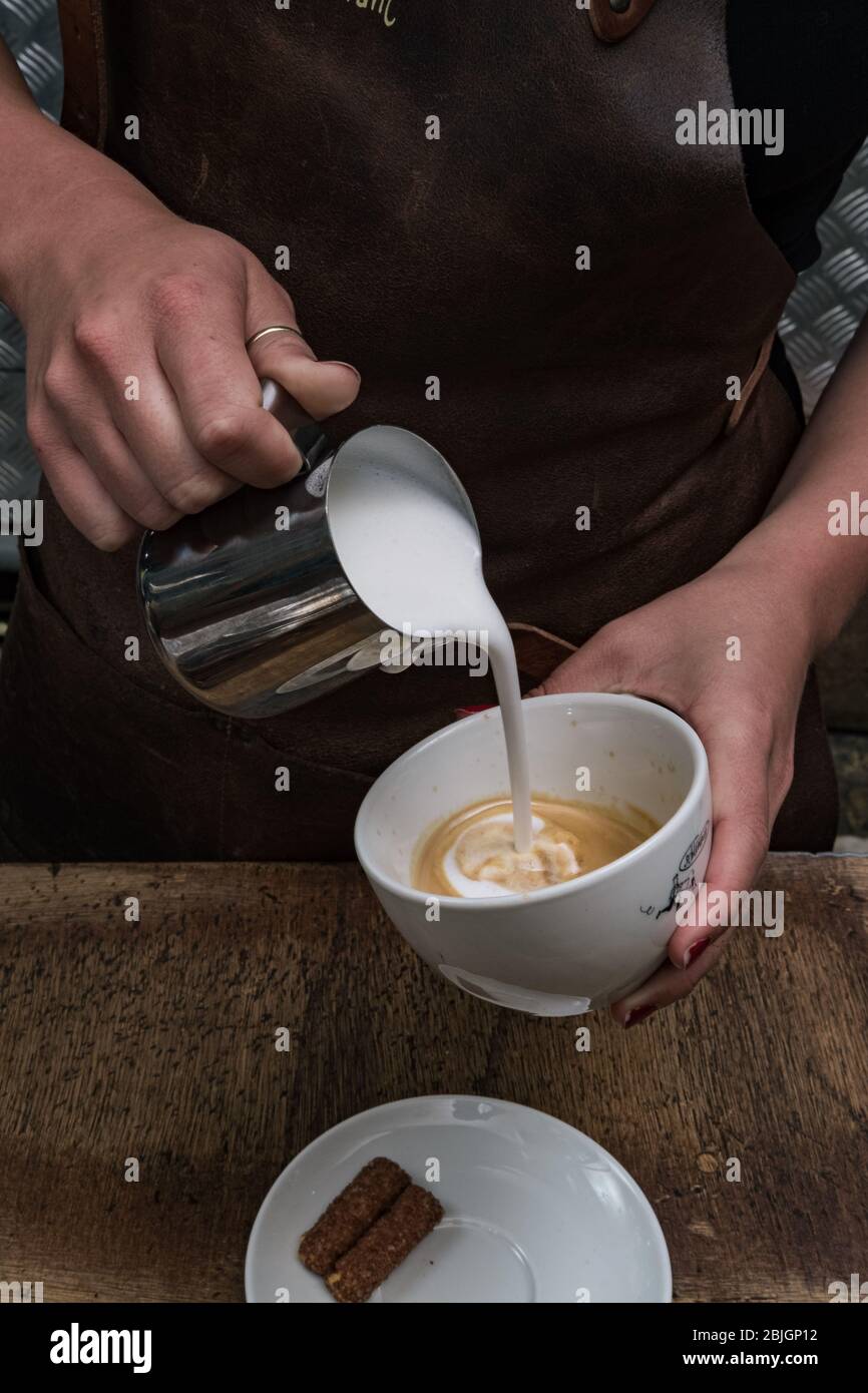 Nahaufnahme von Baristas Händen, die Cappuccino-Kaffee im Café zubereiten. Barista bereitet ein köstliches Morgengetränk zu. Stockfoto