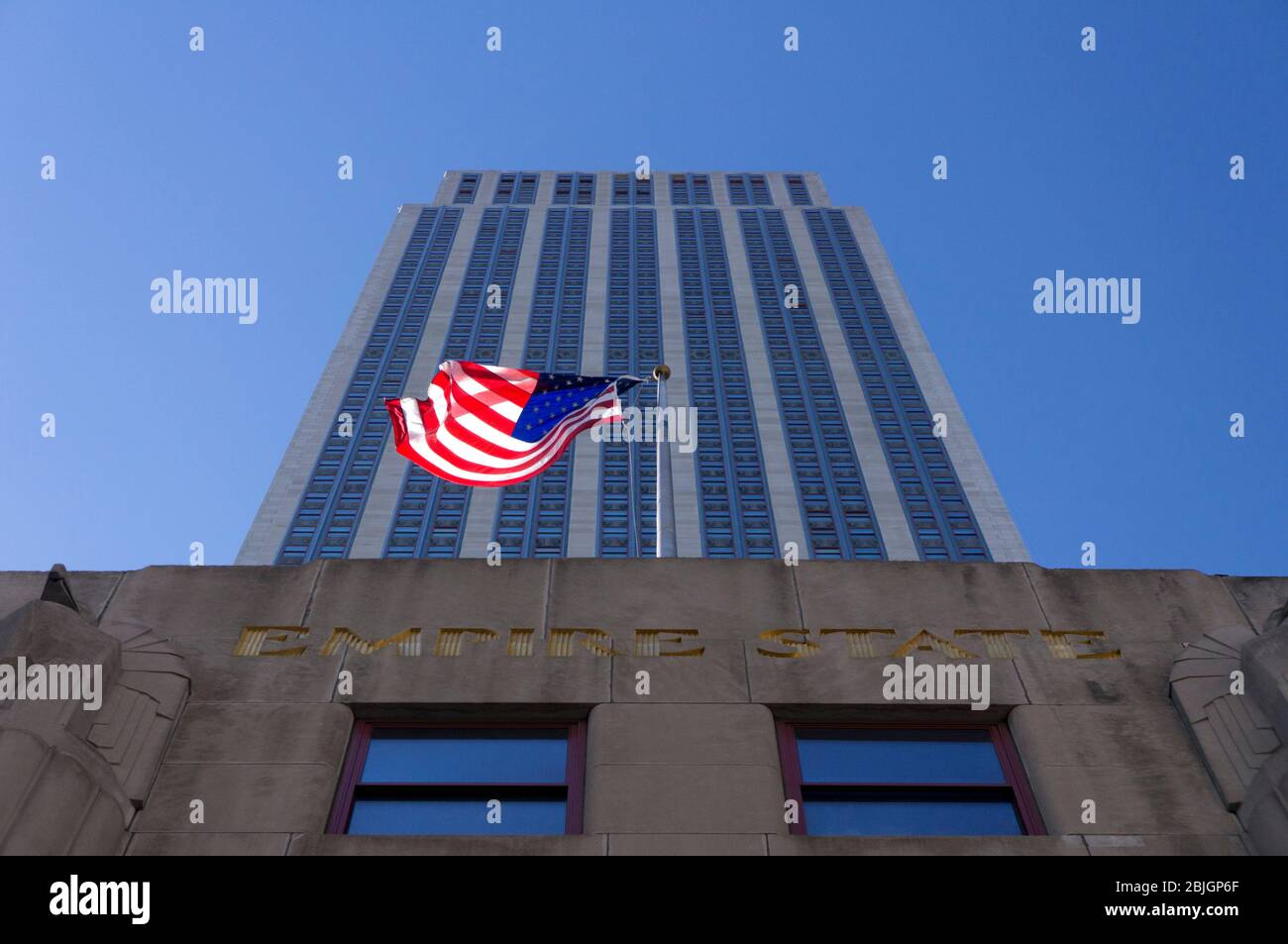 Blick direkt auf das historische Empire State Building mit winkender amerikanischer Flagge in New York City Stockfoto
