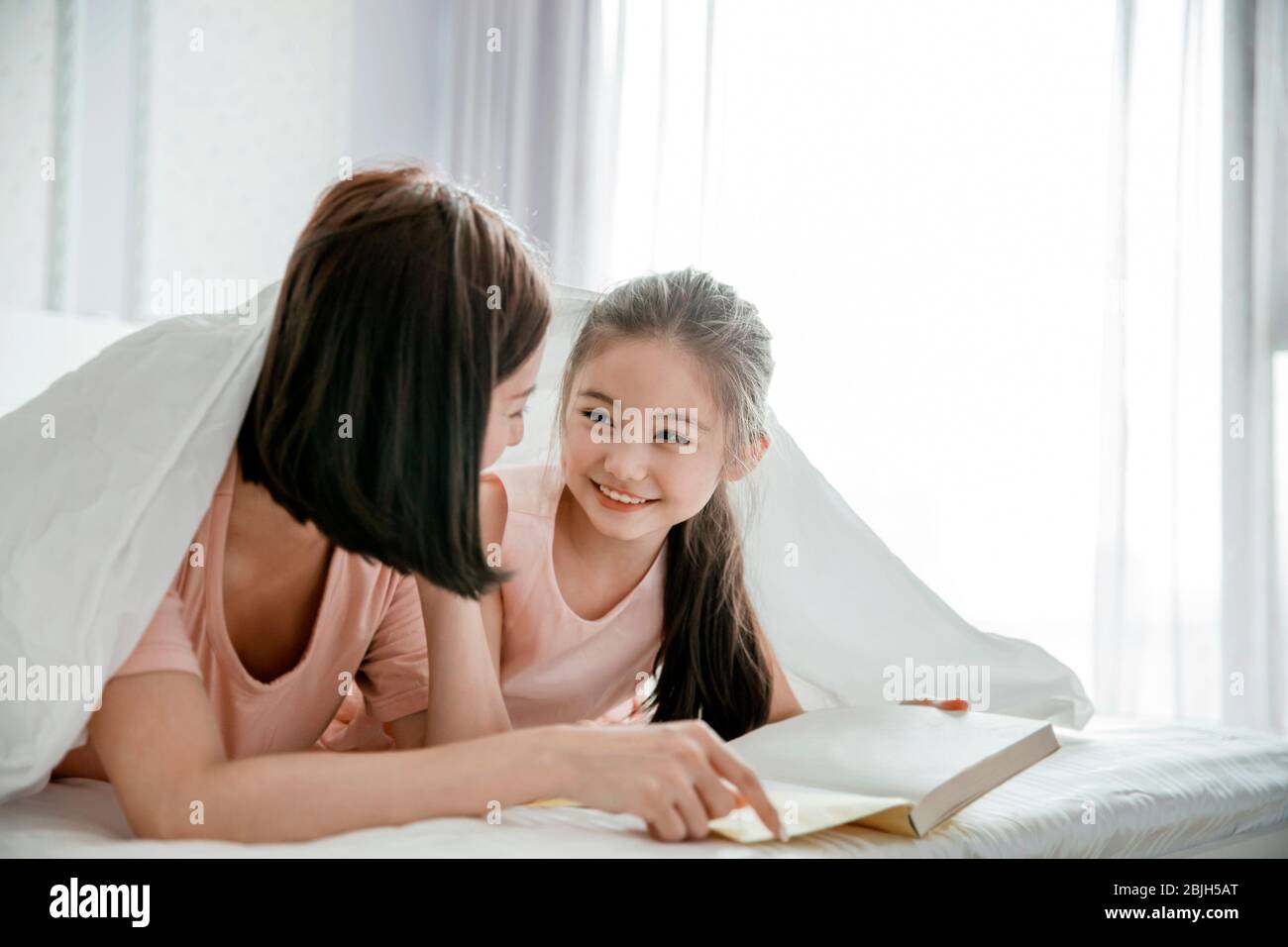Glückliche Mutter und Tochter Kind Buch lesen zusammen im Bett Stockfoto