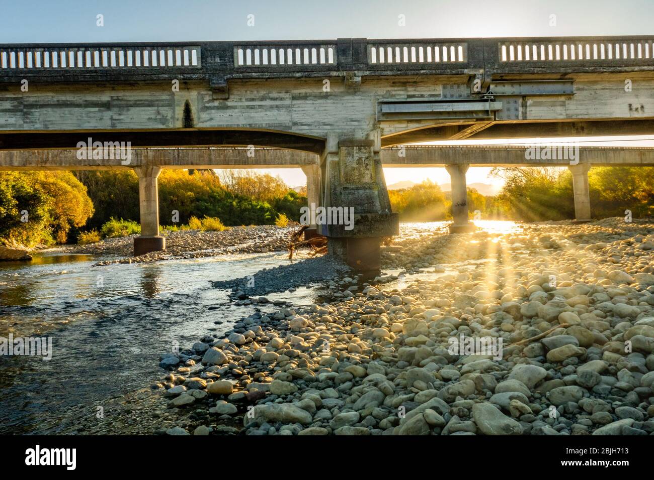 Niedriger Wasserstand im Fluss in ländlicher Landschaft mit einem Sonneneinstrahlung bei Sonnenuntergang unter der Brücke Stockfoto