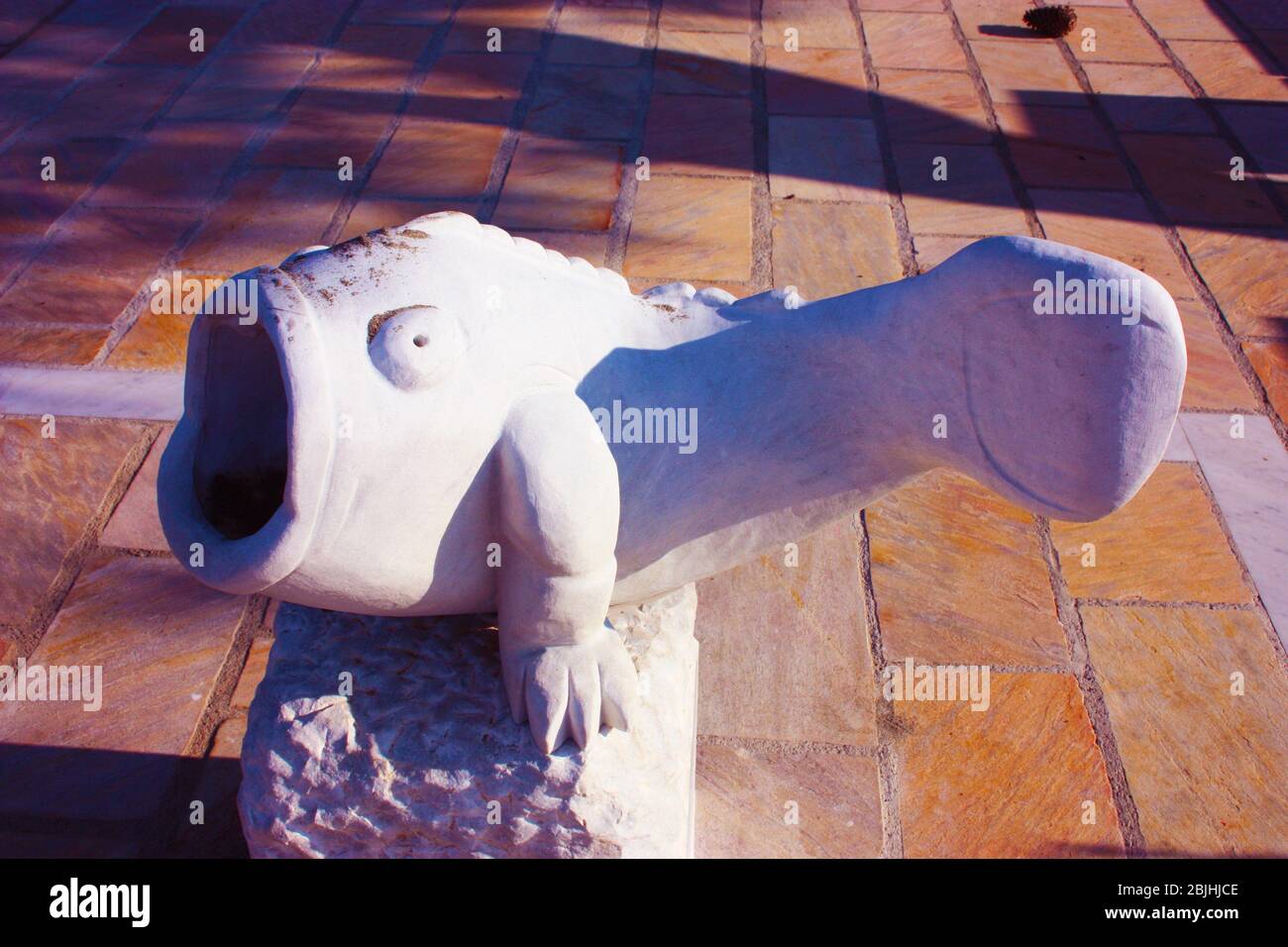 Seltsame Statue in weißem Marmor, die einen fetten Fisch mit einem großen Mund weit offen in einem gefliesten Garten in der toskana darstellt Stockfoto