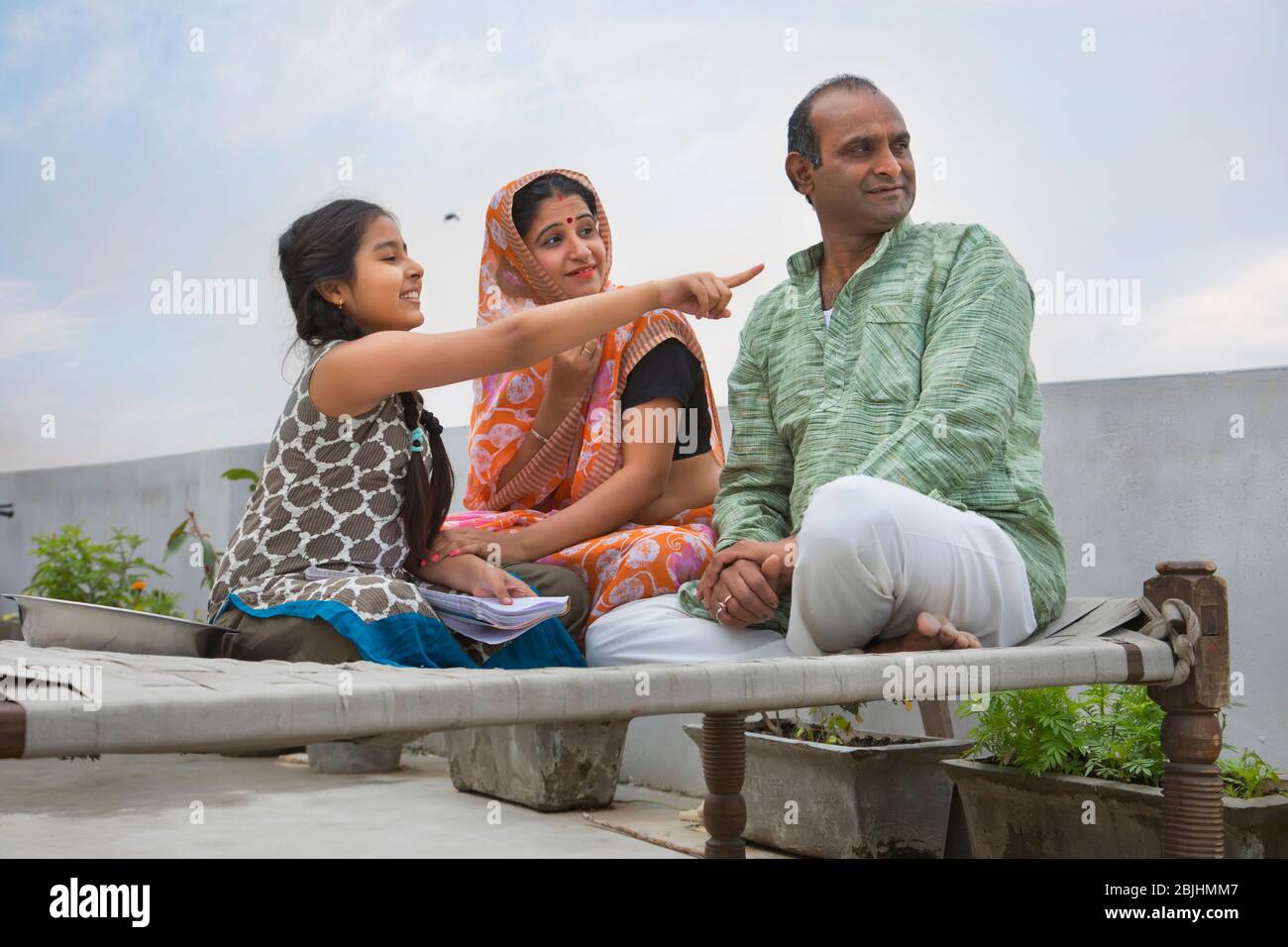 Indische Eltern sitzen auf einem Lager Bett Tochter zeigt etwas Stockfoto