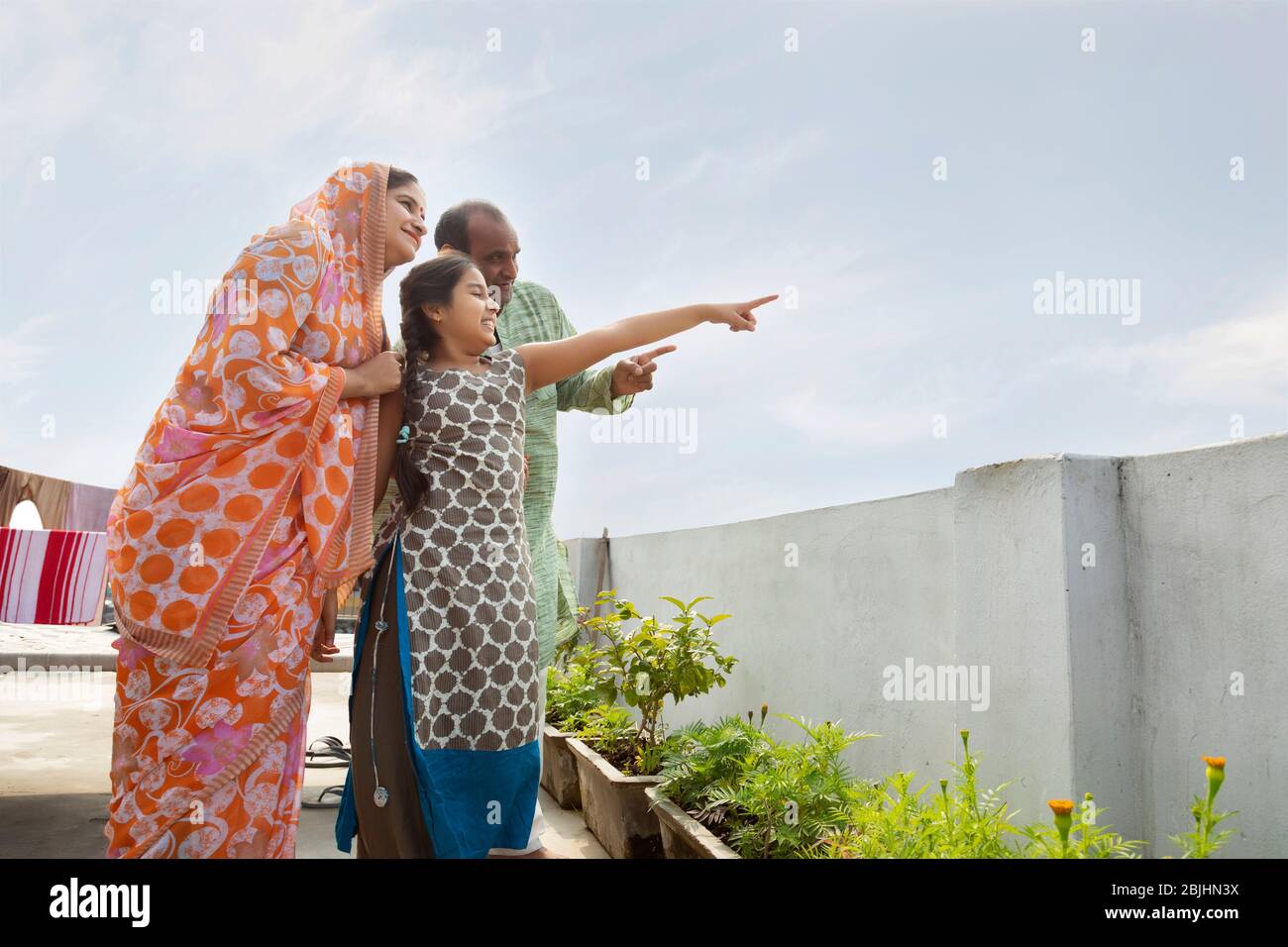 Indische Eltern und Tochter stehen auf dem Dach zusammen zeigen etwas Stockfoto
