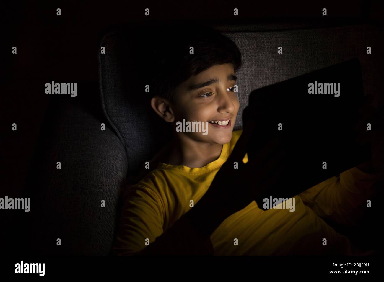 Porträt eines Jungen, der ein Tablet im dunklen Raum benutzt. (Kinder) Stockfoto